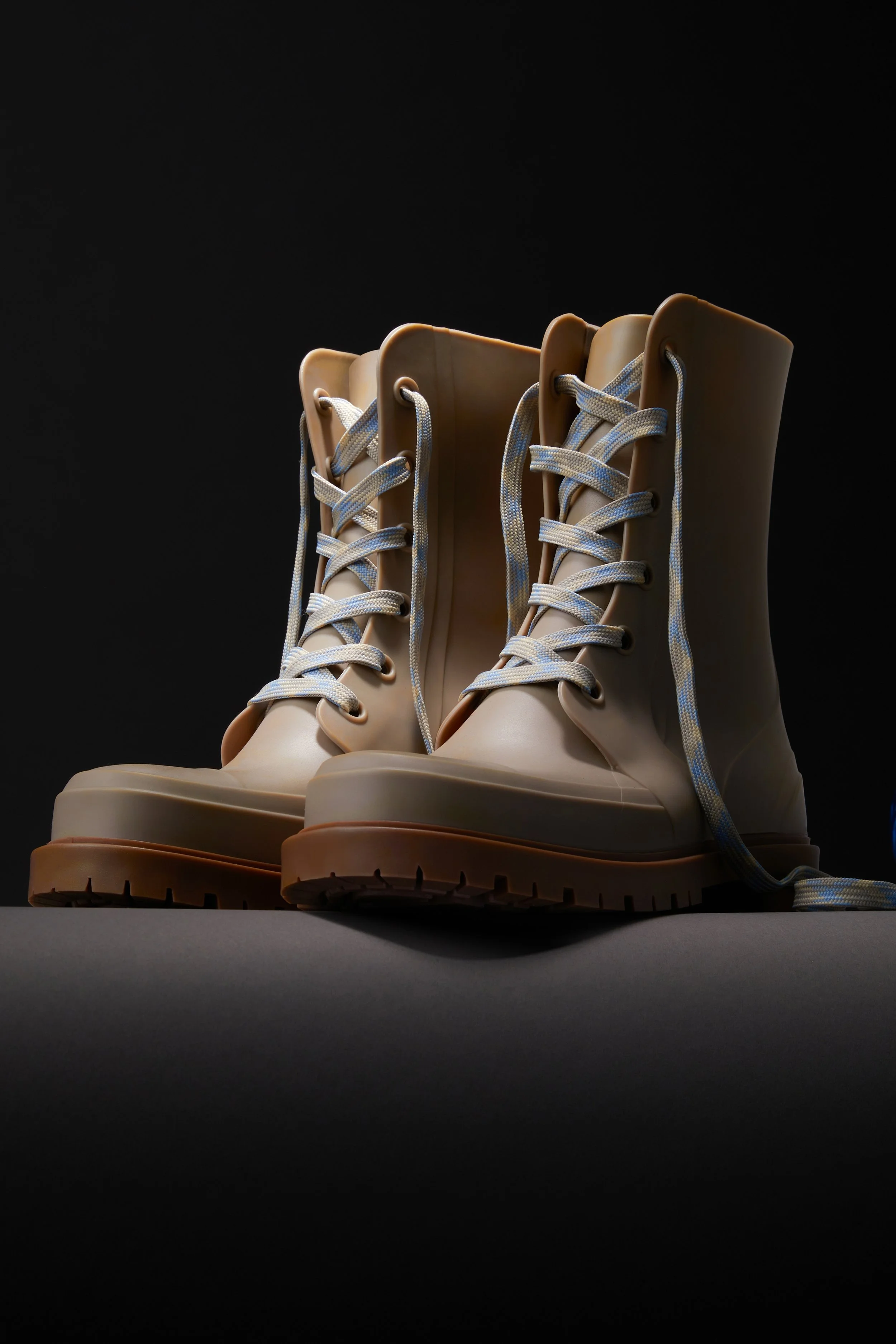 A pair of beige high-top boots with white laces, placed on a dark surface against a black background.