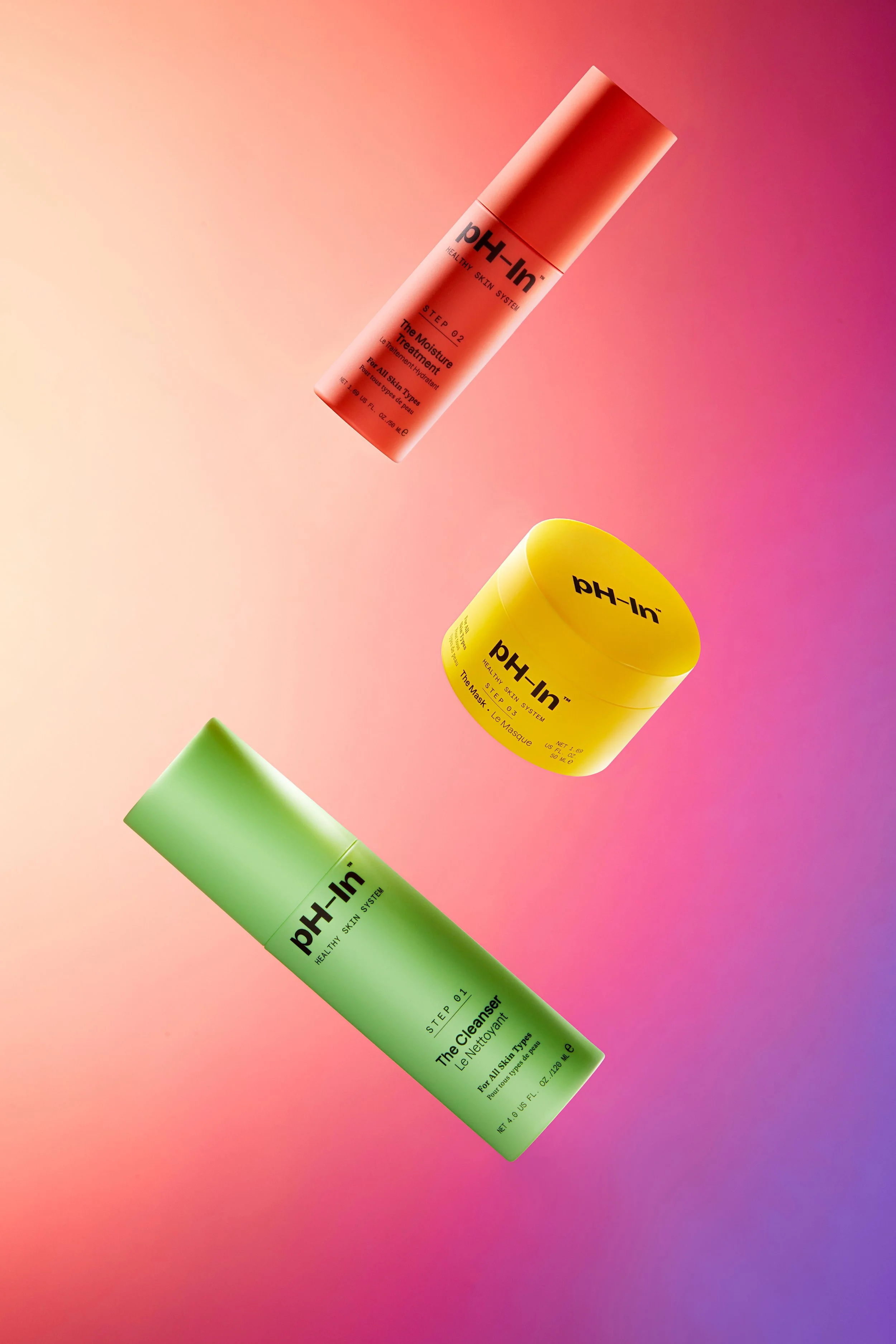 Three skincare products from the pH-In brand, including a pink spray bottle, a yellow jar, and a green tube, floating against a gradient pink and purple background.