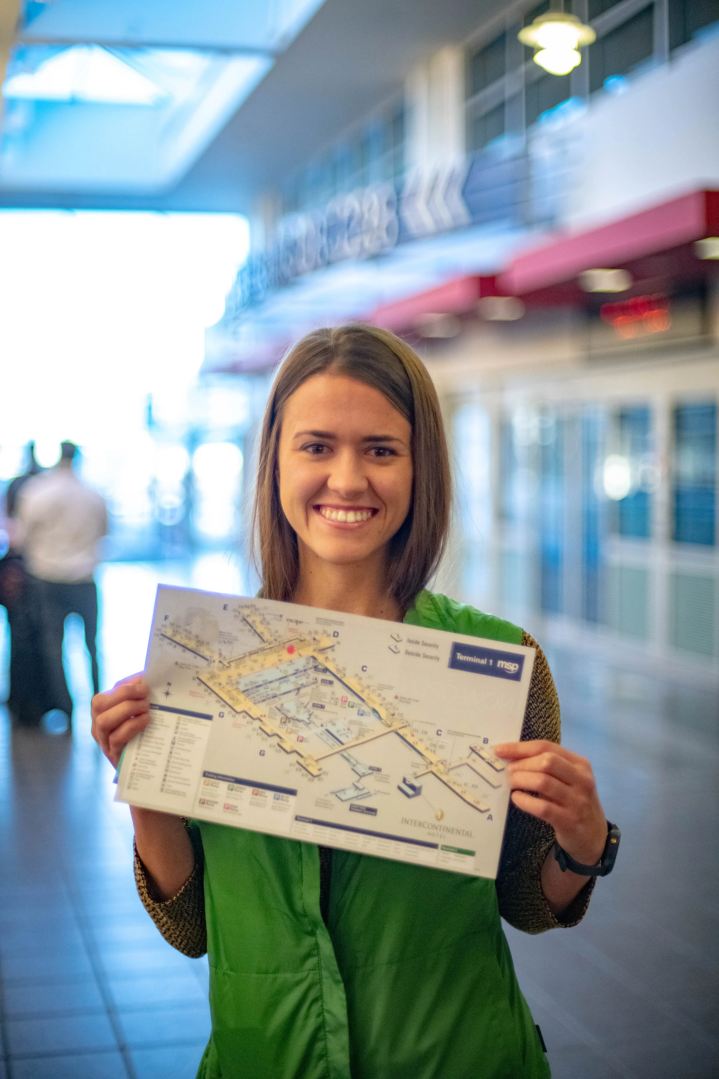 Woman Volunteer smiling at the camera holding up a map of MSP Airports Terminal 1