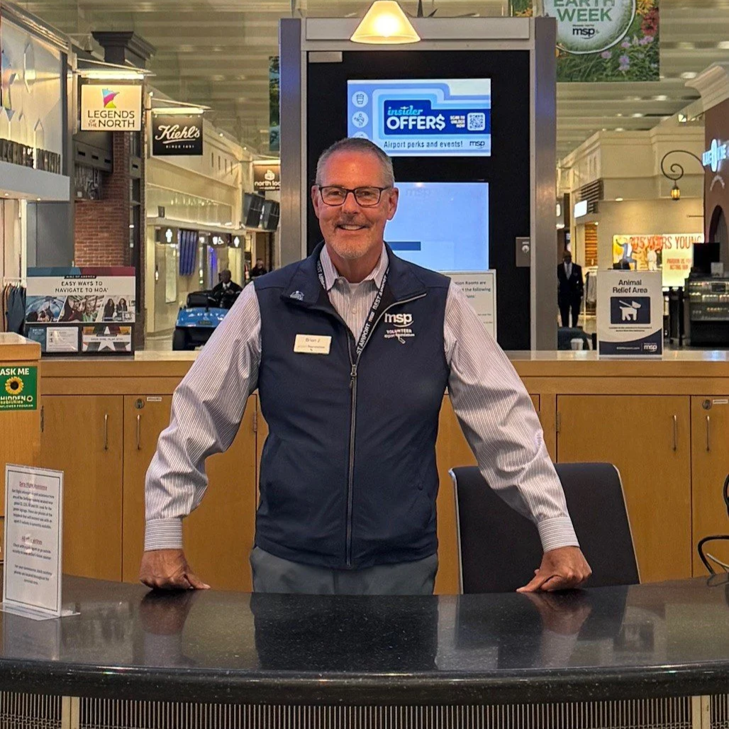 Volunteer smiling behind information booth in main mall of MSP Airport's Terminal 1