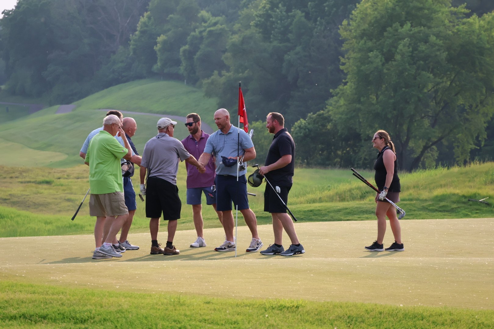 Group of people shaking hands over a hole on a golf course