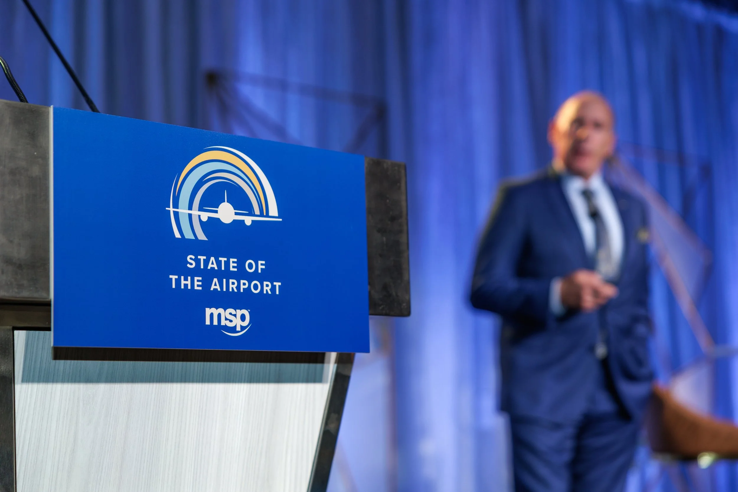 MSP Airport Brian Ryks on stage at the State of the Airport Luncheon with a sign for the event in front of him