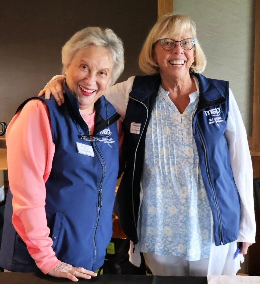 Two volunteers smiling at the camera wearing blue vents