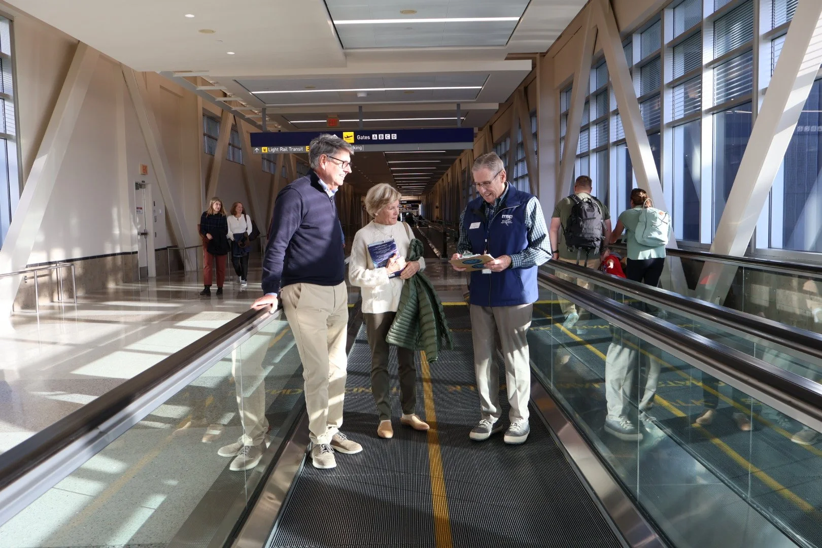 Go Guide male volunteer walking with two travelers on a moving walkway