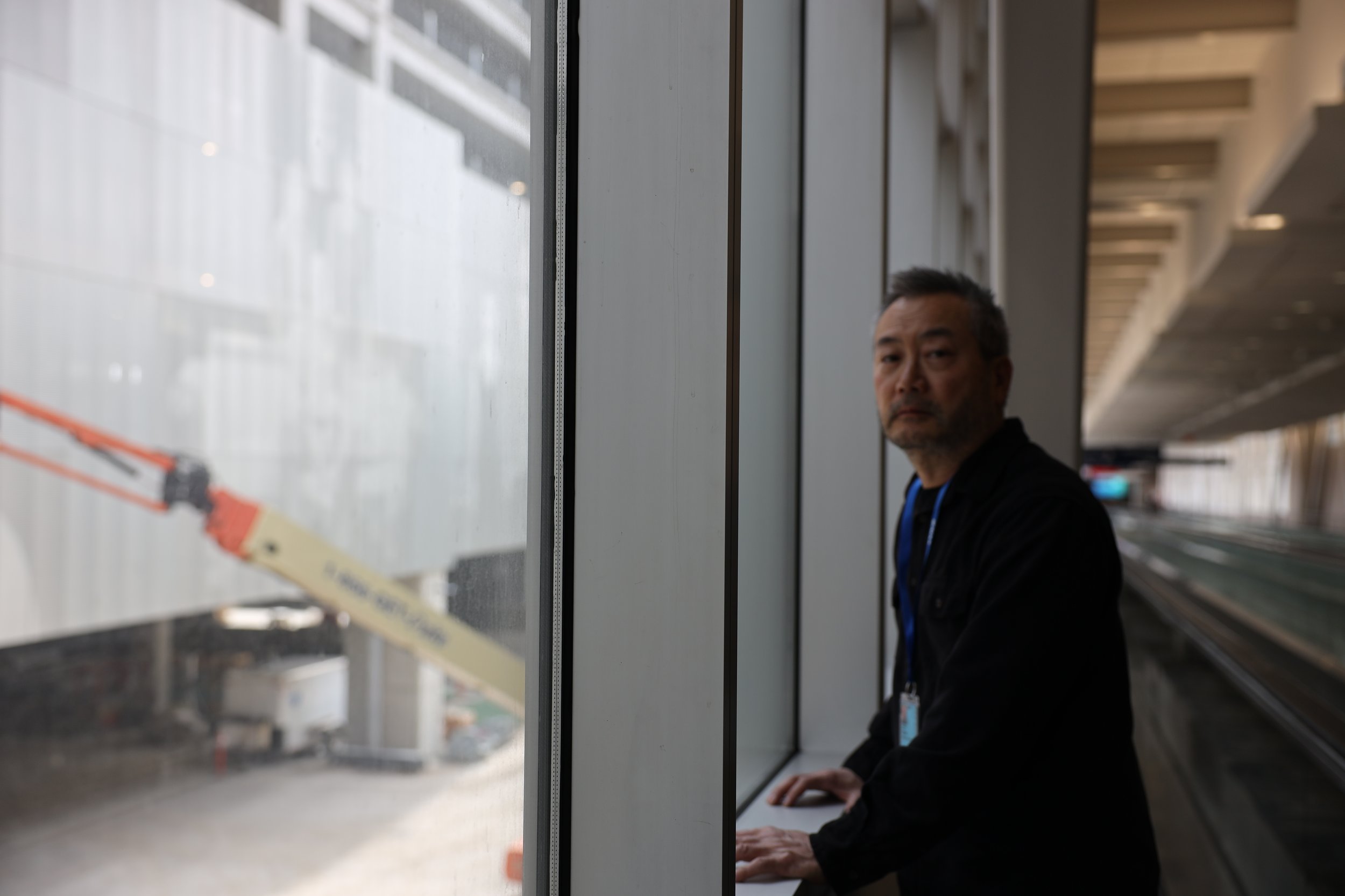 Artist Steve Ozone standing in front of the window that looks out to his artwork titled "Interrupted Landscapes of the Incomer"