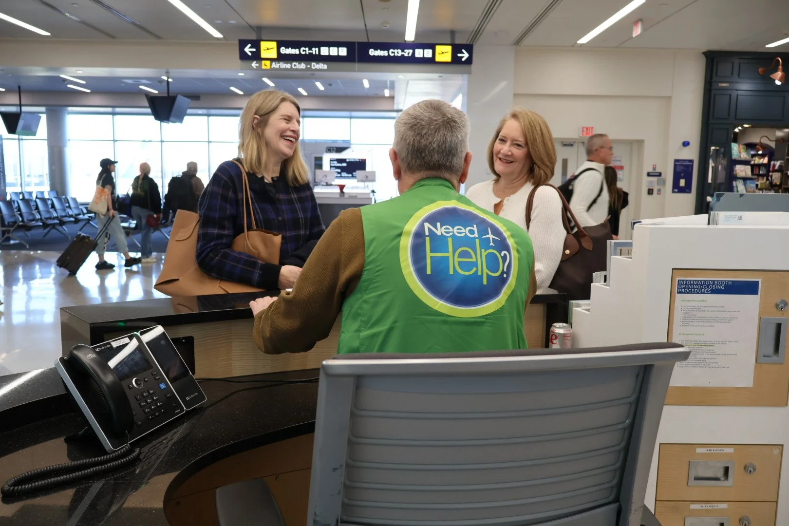 Volunteer sitting at an information booth talking with two travelers on the other side of the booth