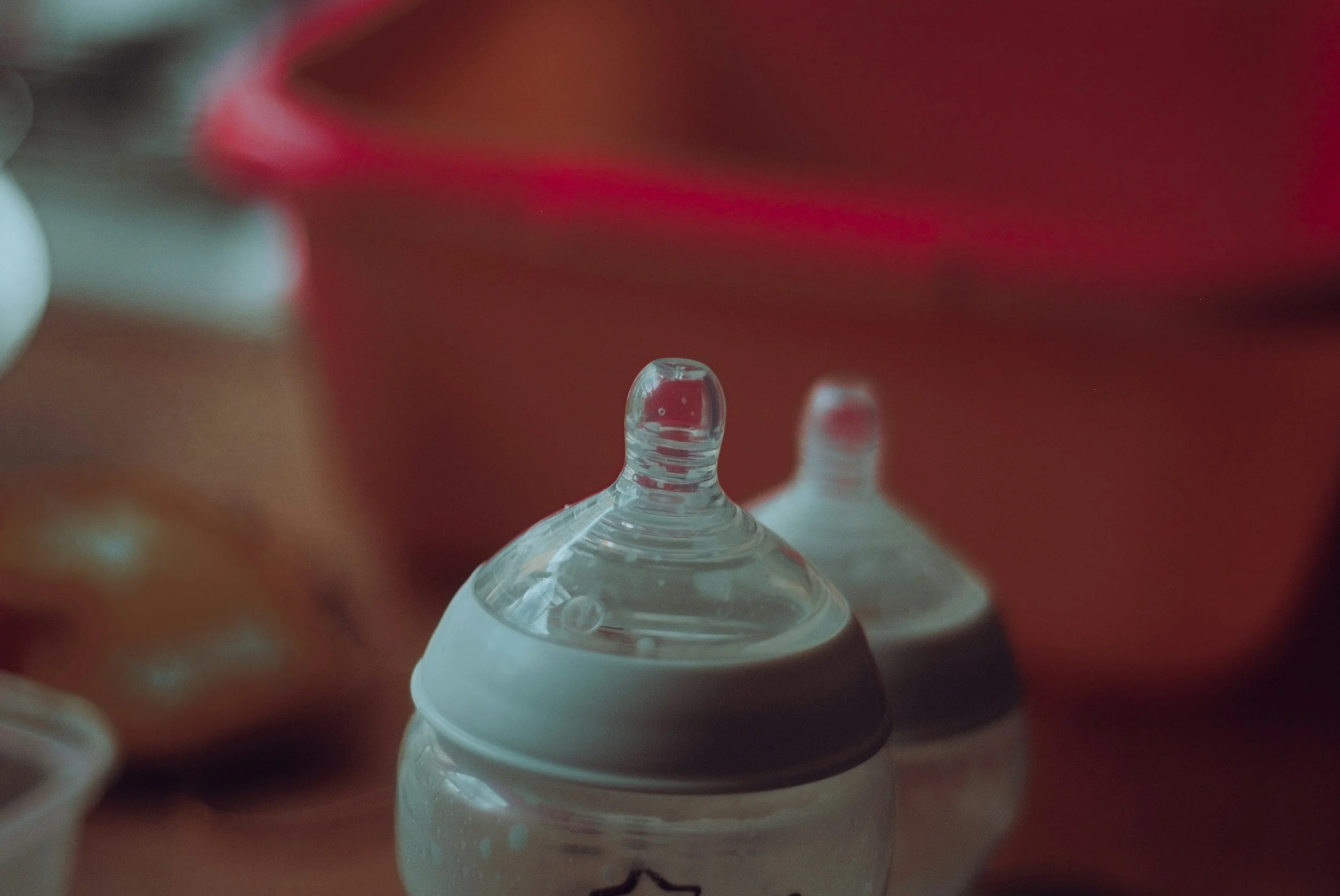 Close-up of a baby bottle nipple with a blurred background of other baby bottles and containers.