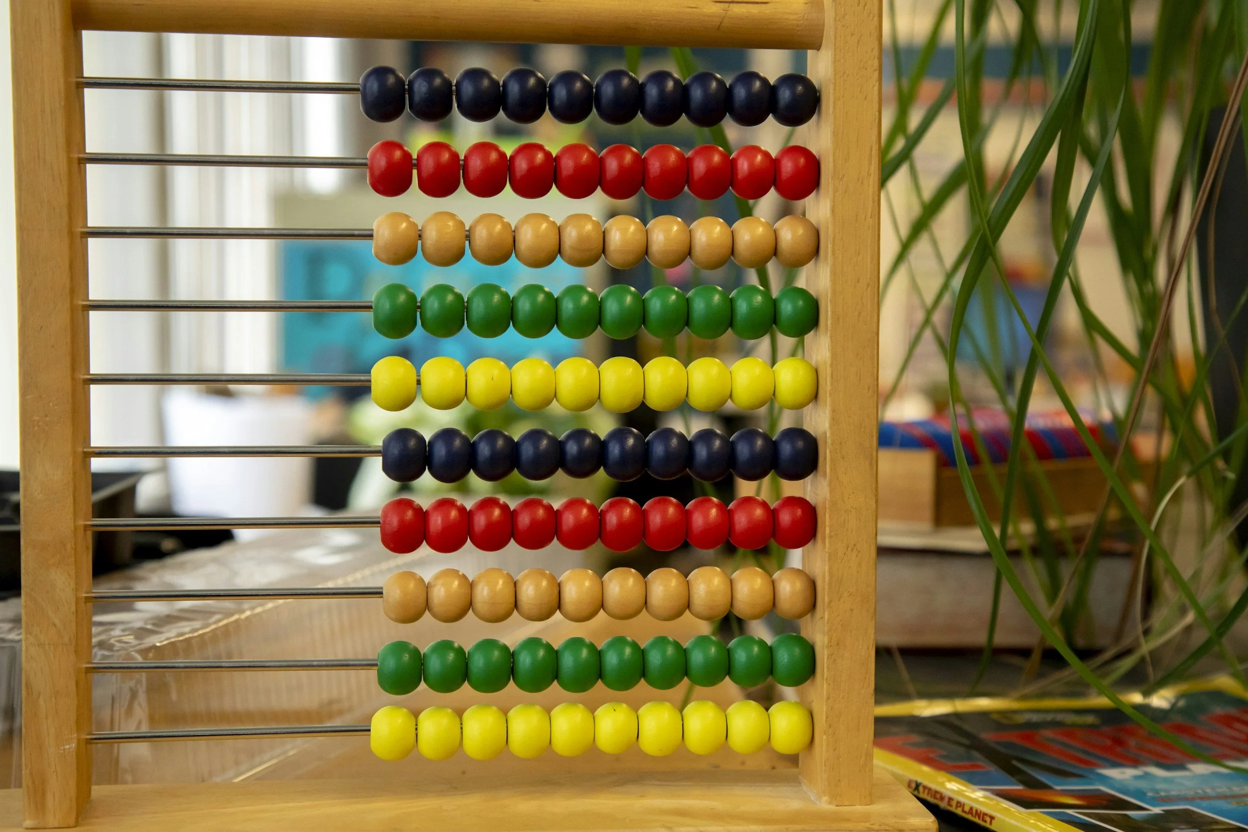 A wooden abacus with colorful beads in red, black, yellow, green, and beige, arranged on metal rods.