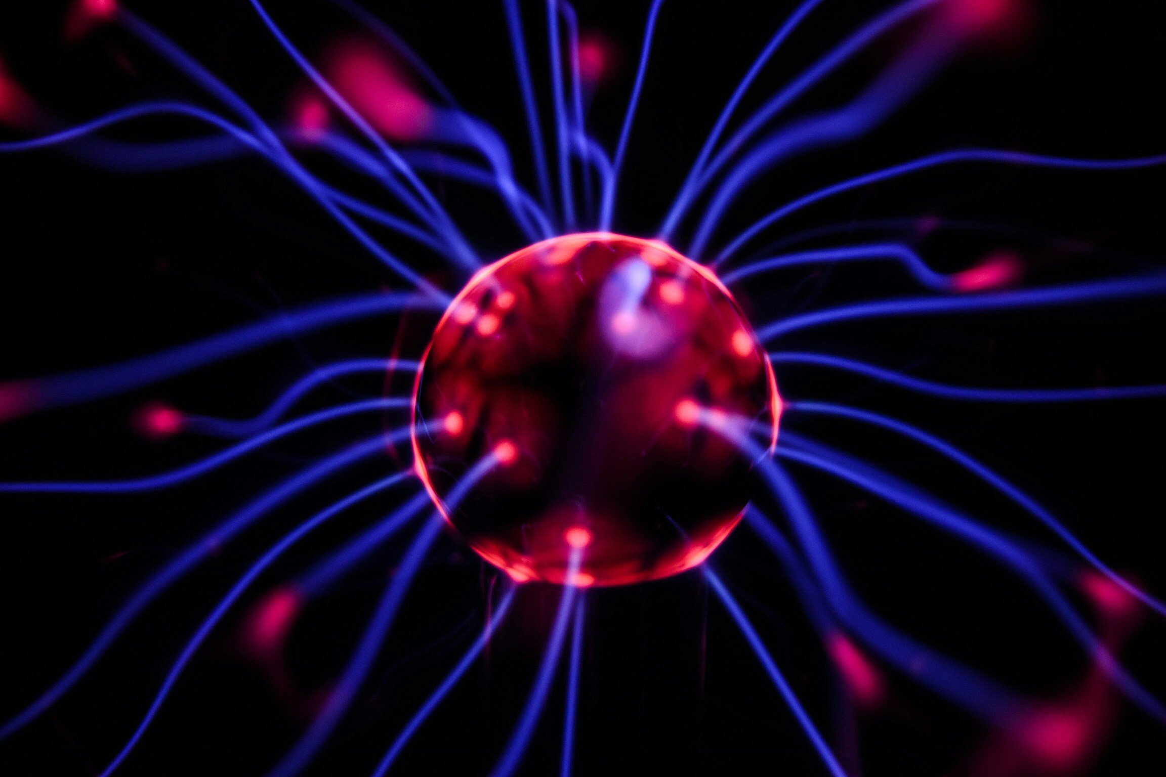 Close-up of a plasma globe with pink and blue electric filaments emanating from the center in a dark background.