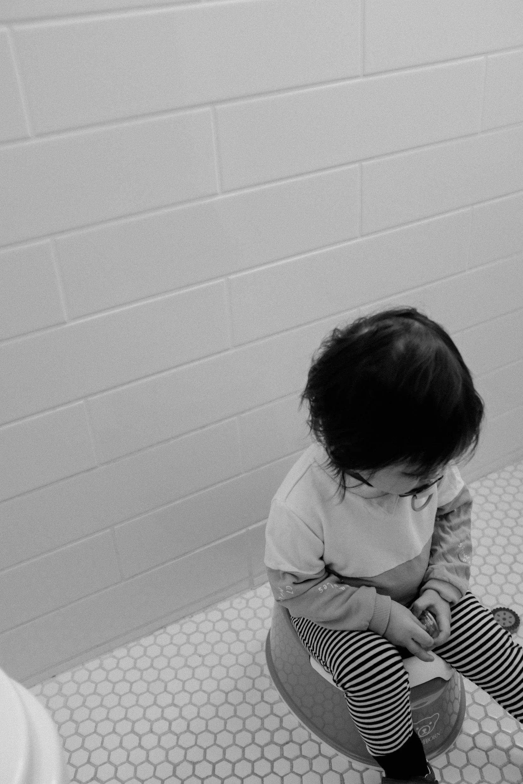 A young child with glasses sitting on a potty in a tiled bathroom.