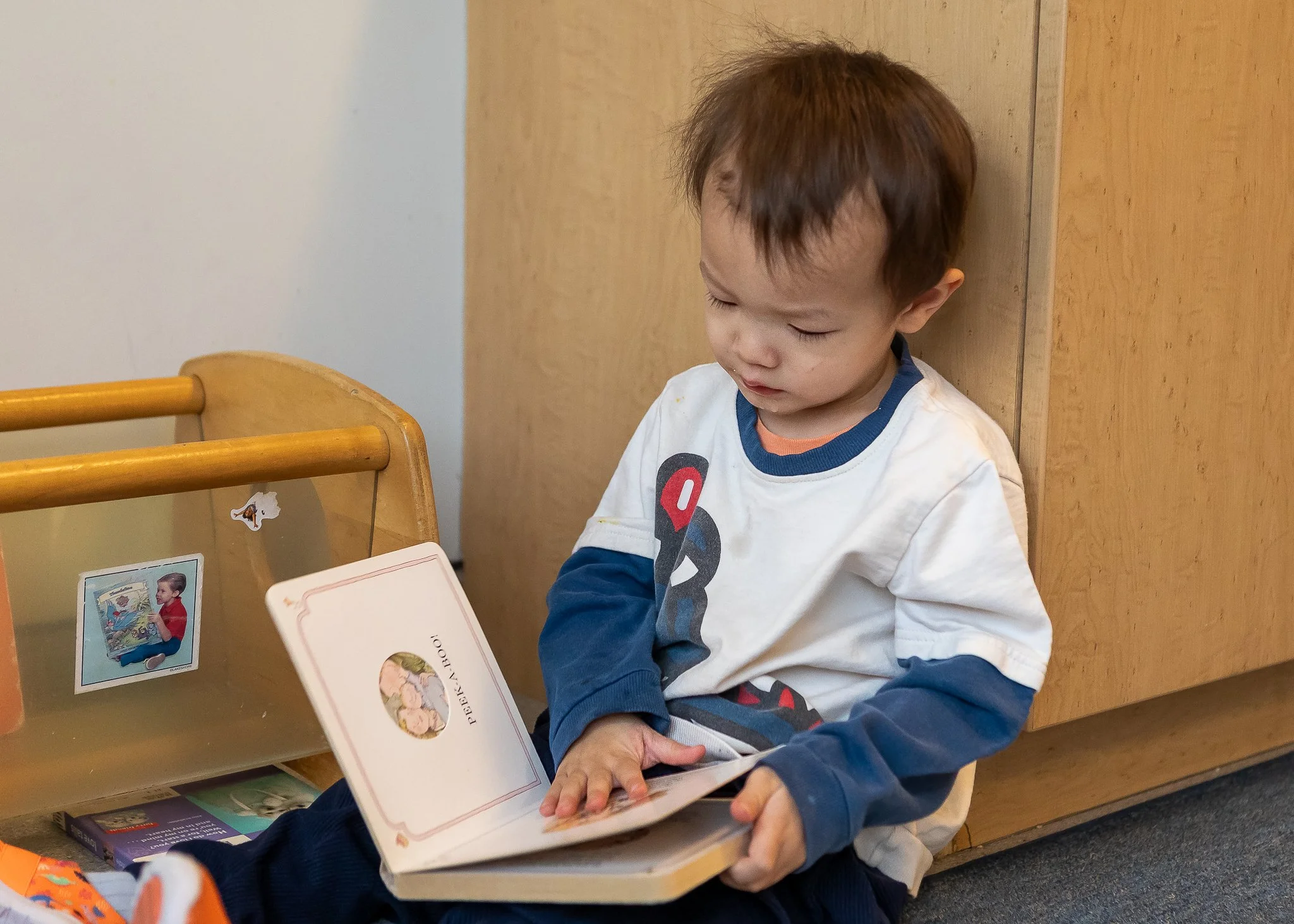 A young girl sitting at a wooden table, reading a Dr. Seuss book titled 'Hop on Pop' in a brightly lit room.