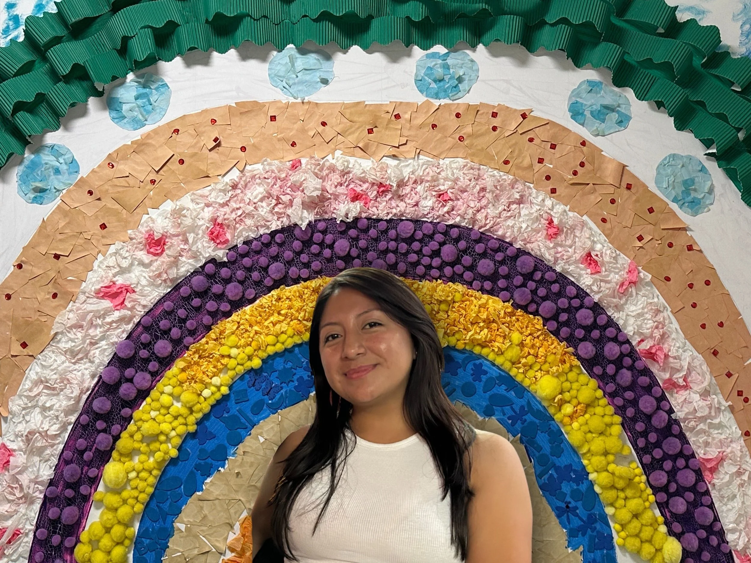 A woman standing in front of a colorful rainbow art installation made of various textured materials.