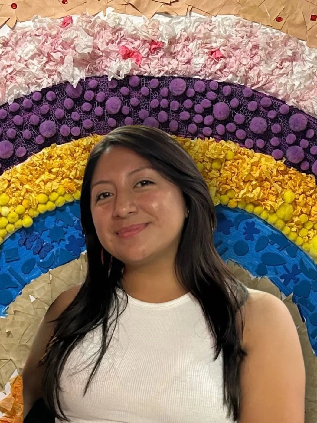 A woman standing in front of a colorful rainbow art installation made of various textured materials.