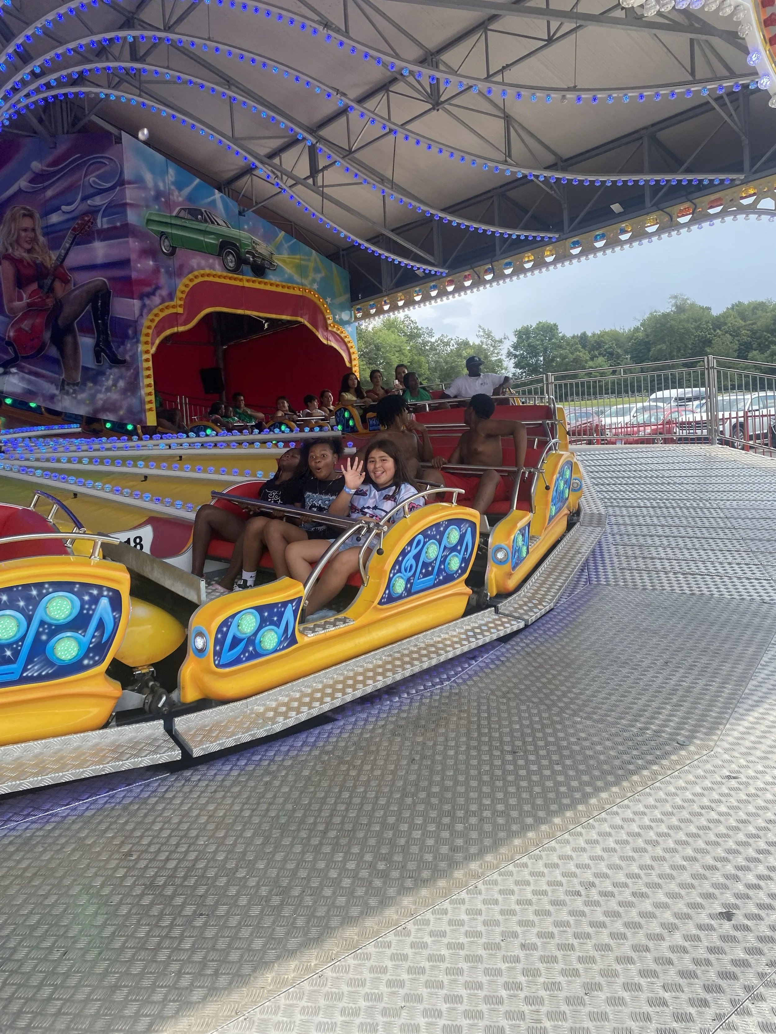 Close-up of the front of a yellow school bus with red warning lights on, an emergency door sign, and tinted windows. Clear blue sky in the background.