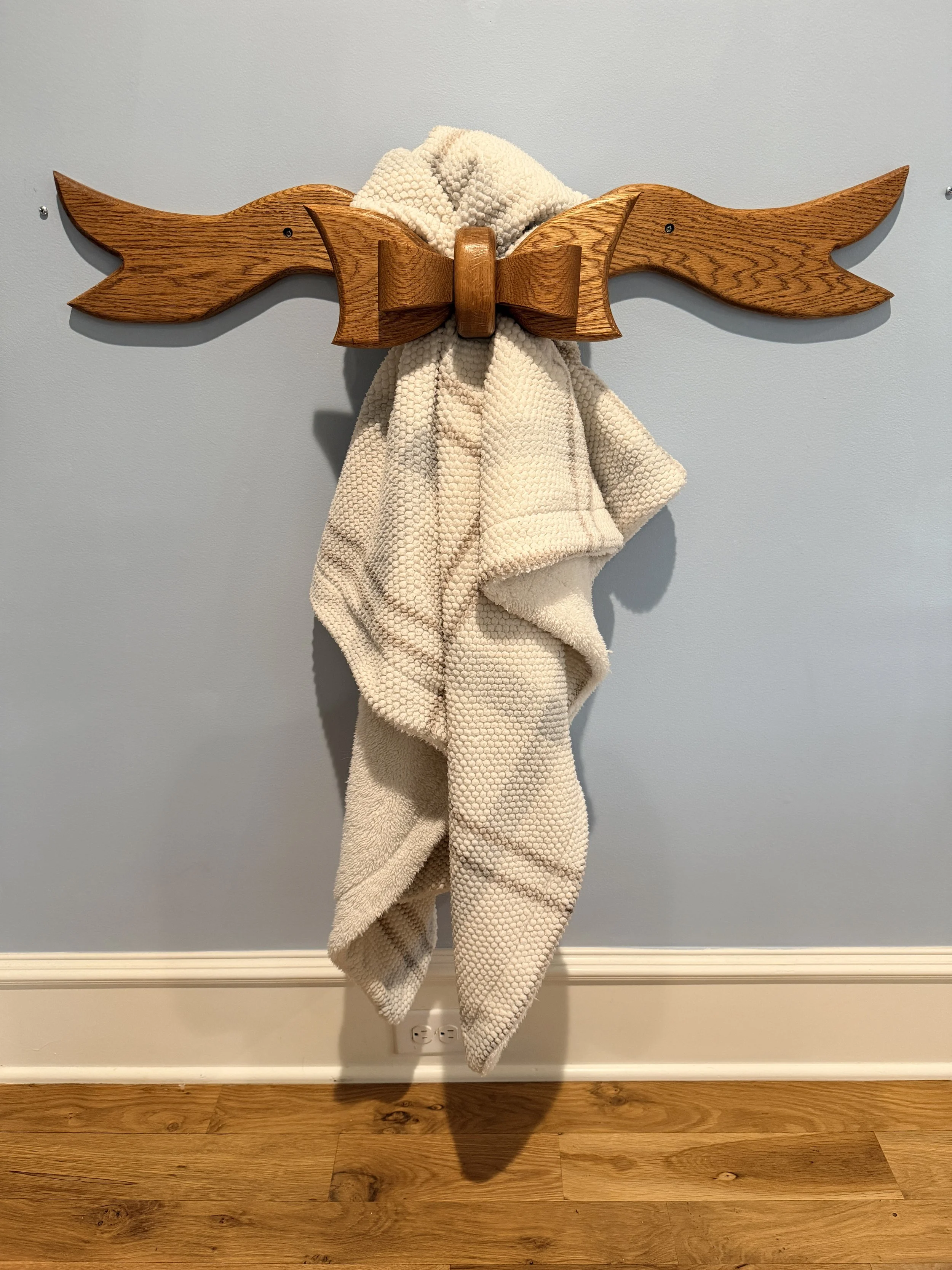 Wooden wall hook in the shape of dragon wings with a beige towel hanging from it, mounted on a pale blue wall.