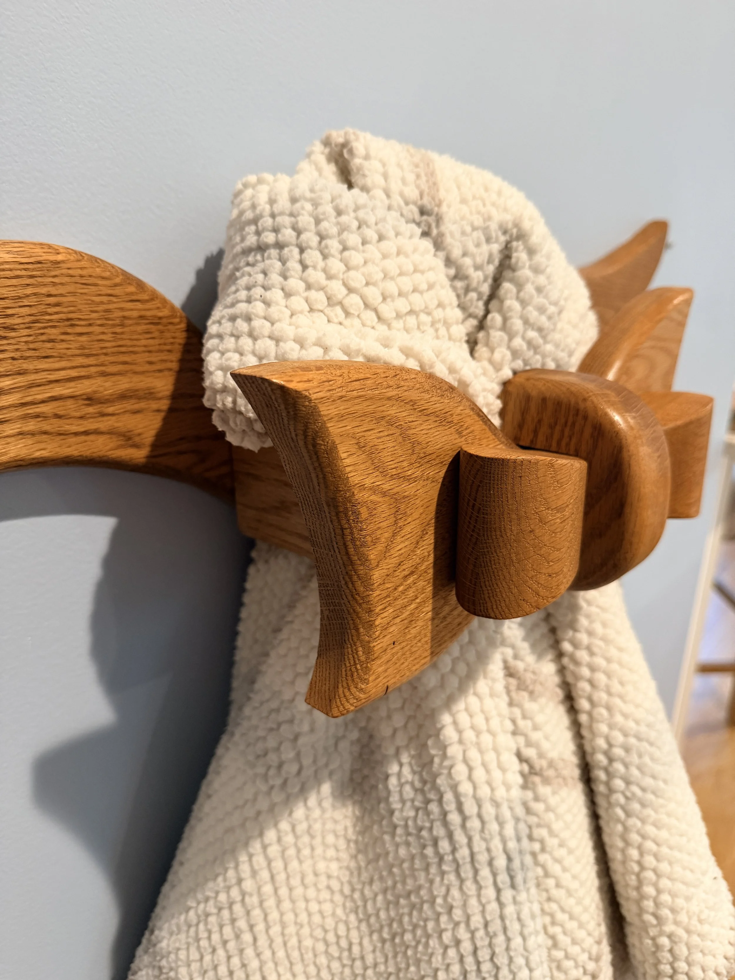 Close-up of a wooden coat hook with a textured cream-colored blanket hanging on it, against a light blue wall.