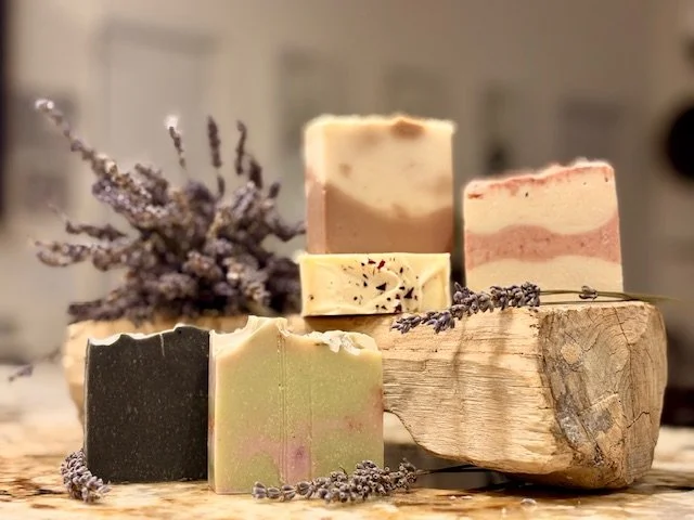 Various handmade soap bars arranged on a rustic wooden surface with lavender sprigs.