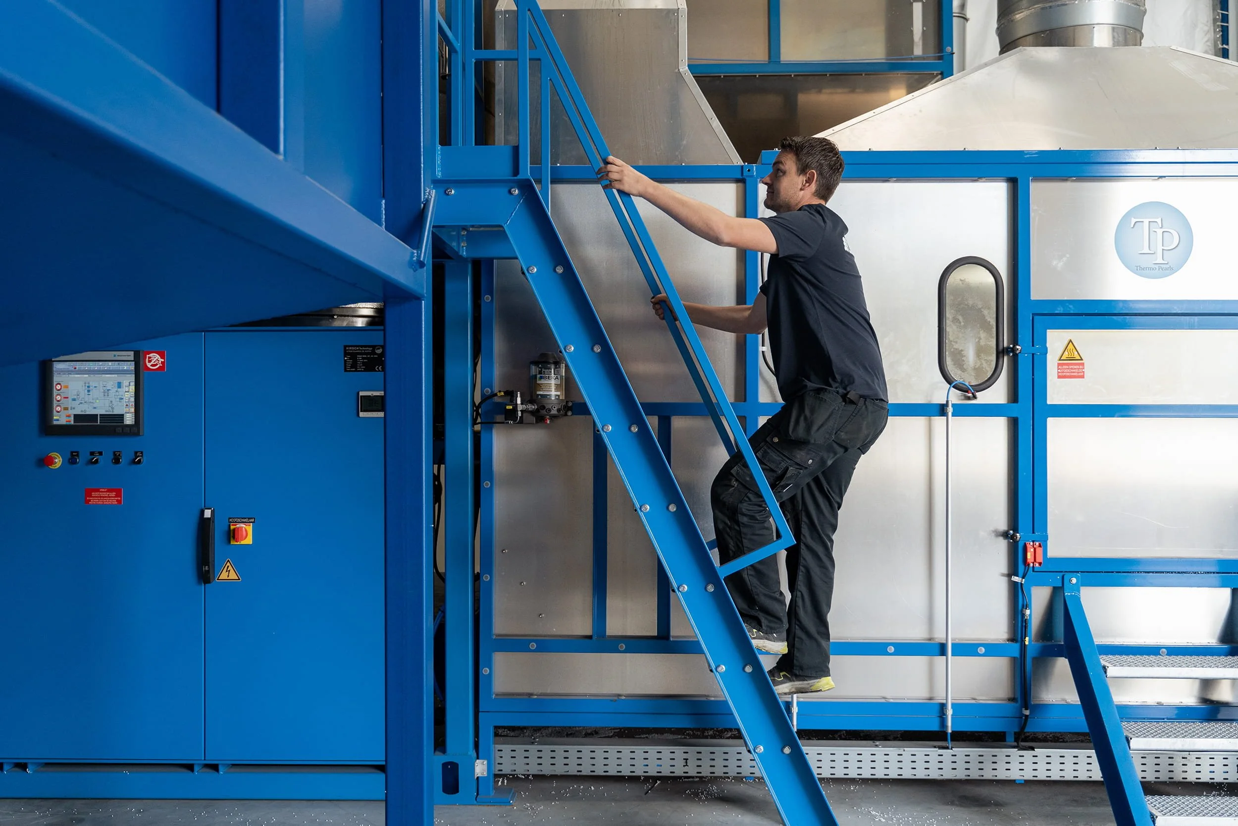Employé de Ludiso montant un escalier métallique à côté d’une machine bleue dans l’usine.