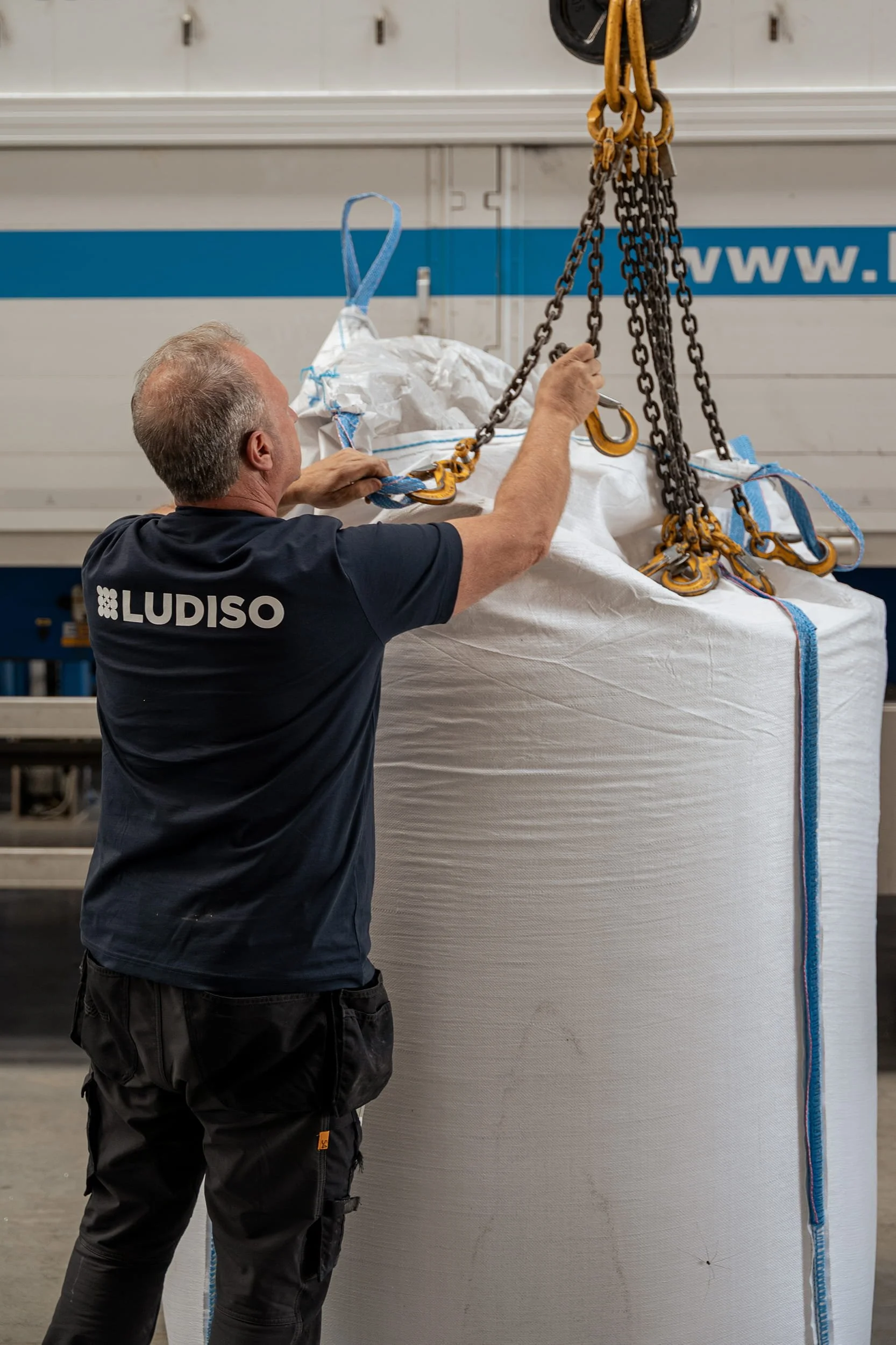 Employé de Ludiso fixant des chaînes à un grand Big Bag rempli de produits isolants dans l’atelier de production.