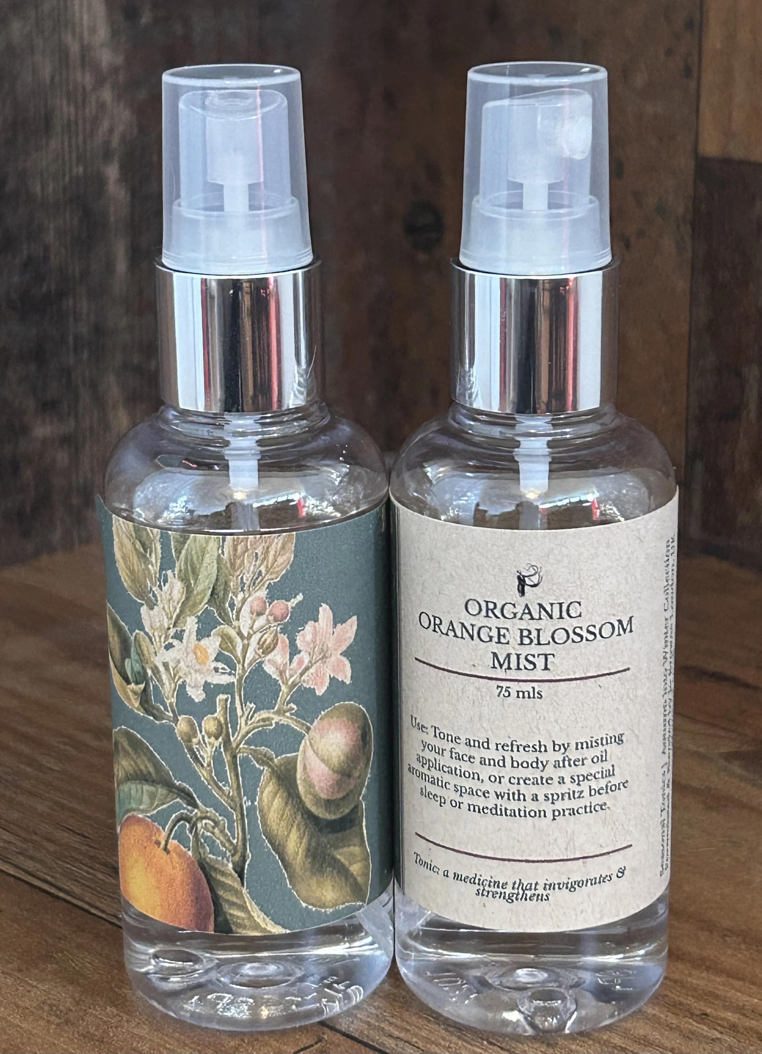 Two spray bottles with labels; one features an illustration of orange blossoms, and the other labeled 'Organic Orange Blossom Mist' with instructions for use.