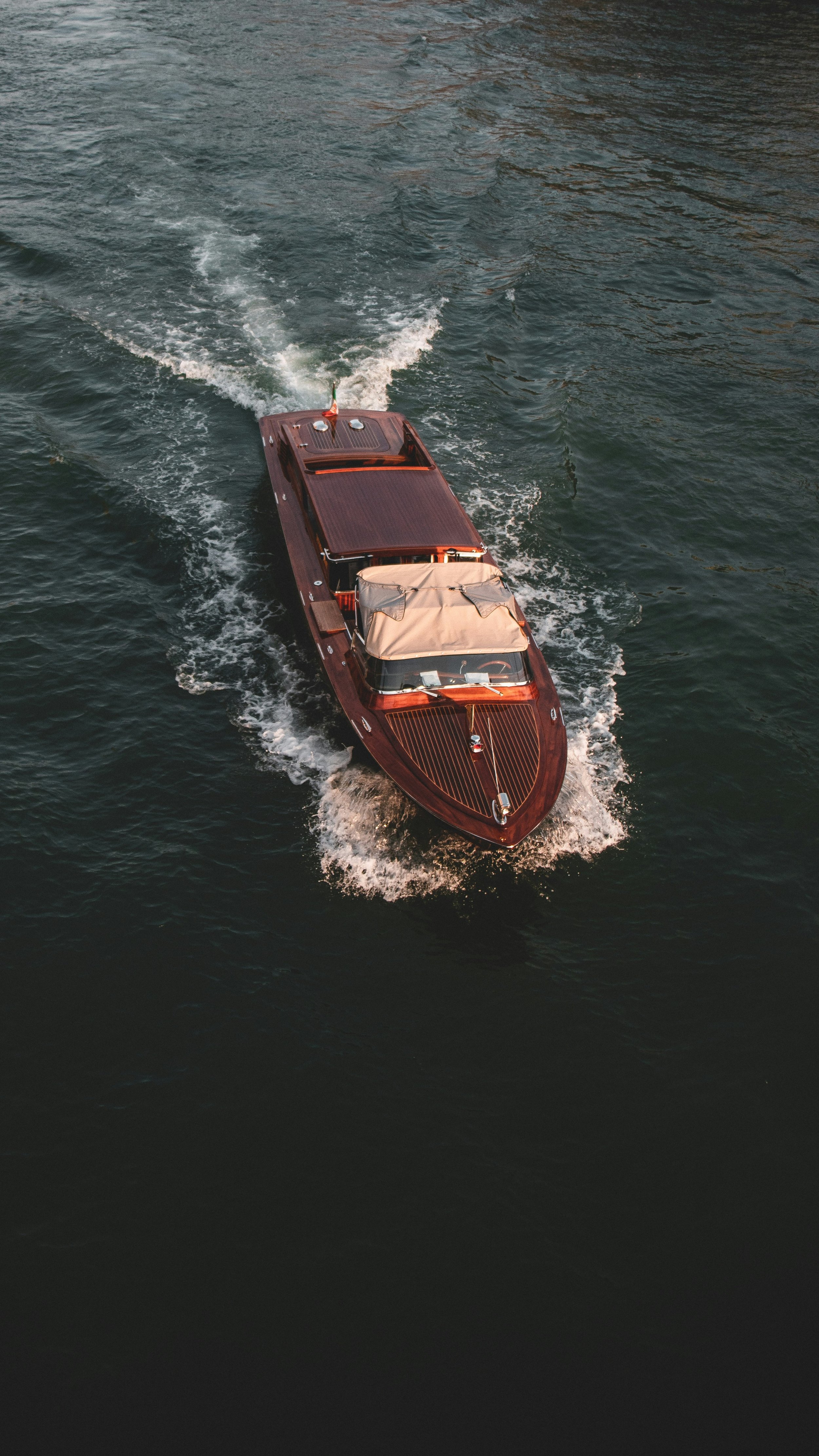 Aerial view of a sleek wooden speedboat moving through water, creating a wake behind it.