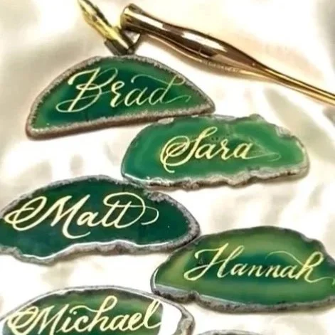 Four custom-made green rock candies with gold script names: Brad, Sara, Matt, Hannah, Michael. A gold pen is placed above the candies.