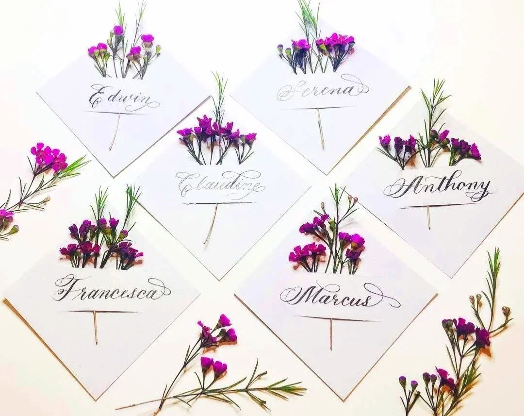 Name cards with handwritten calligraphy and small purple flowers, each representing a different name.