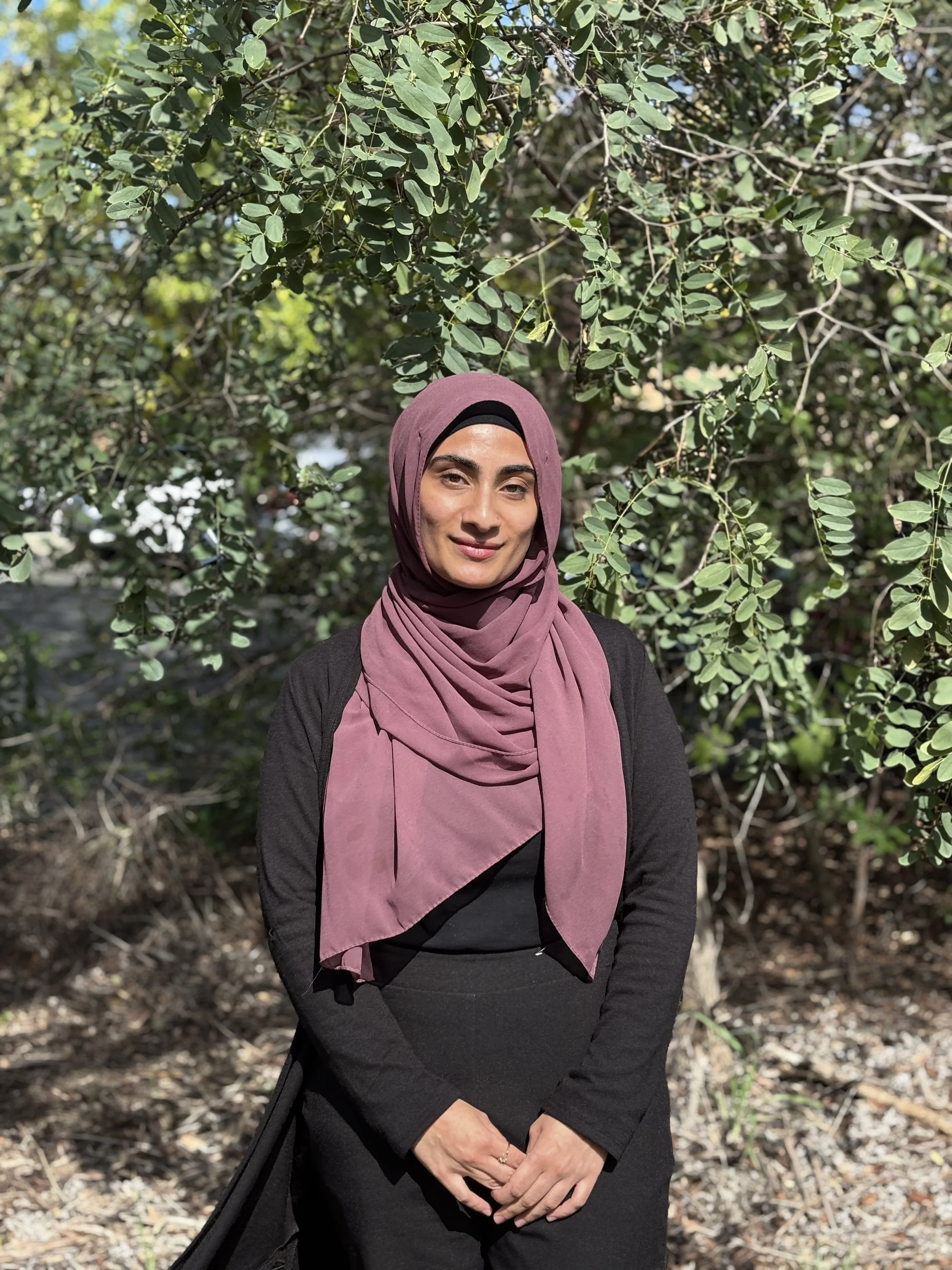 A woman wearing a beige headscarf and brown sweater, sitting in front of a background of colorful tulips.