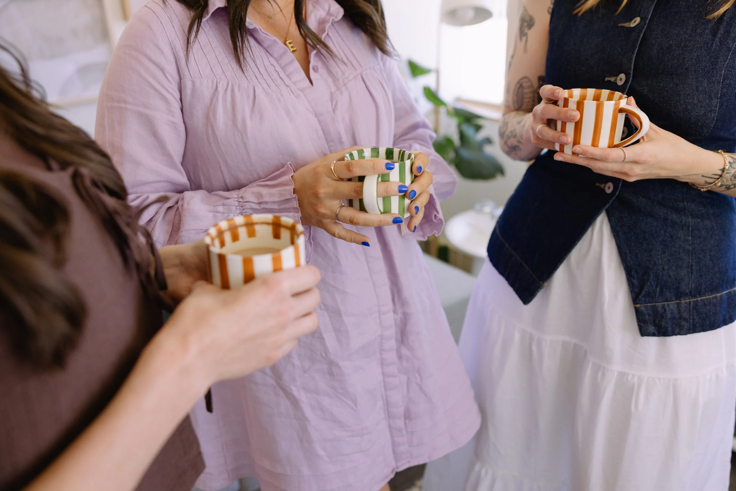 Three women holding coffee cups talk. Image focused on the cups.