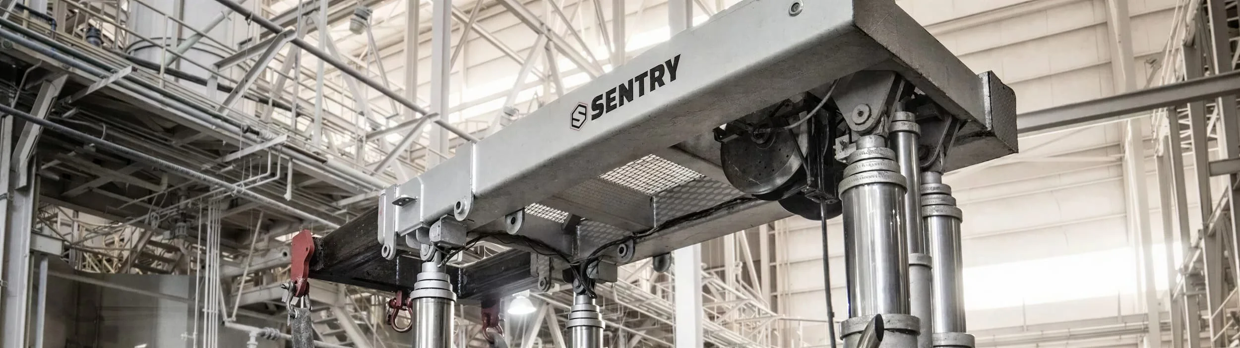 Industrial robotic component labeled 'Sentry' with metal framework, pistons, and wiring inside a factory or warehouse.