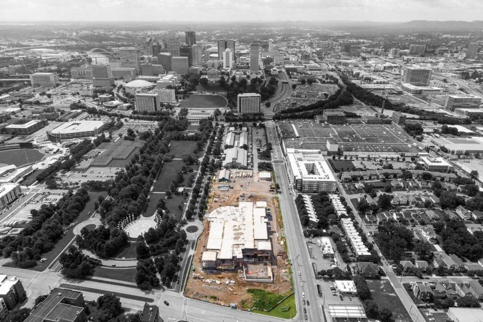 Aerial view of a city skyline with high-rise buildings, a mix of green parks, and a construction site in the foreground.