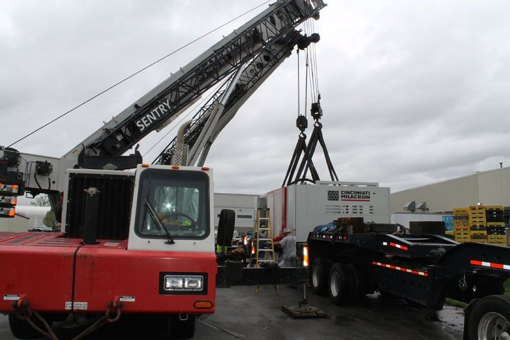A crane lifting a large industrial generator labeled Cincinnati Milacron outdoors on a cloudy day.