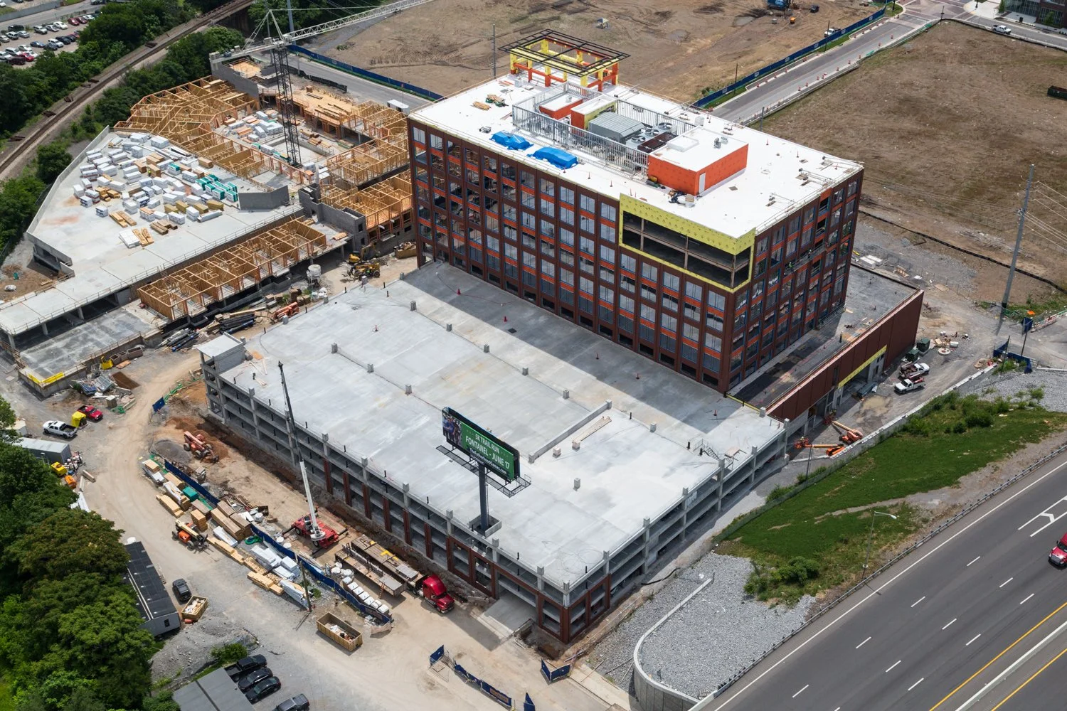 Aerial view of a multi-story building under construction with areas for windows and roof top equipment, construction materials, and vehicles around the site.