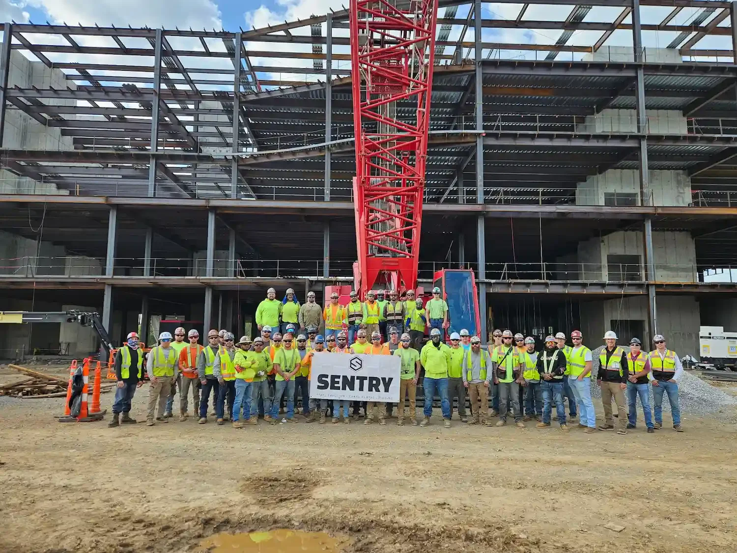 Construction crew in safety vests holding SENTRY banner before steel-framed building