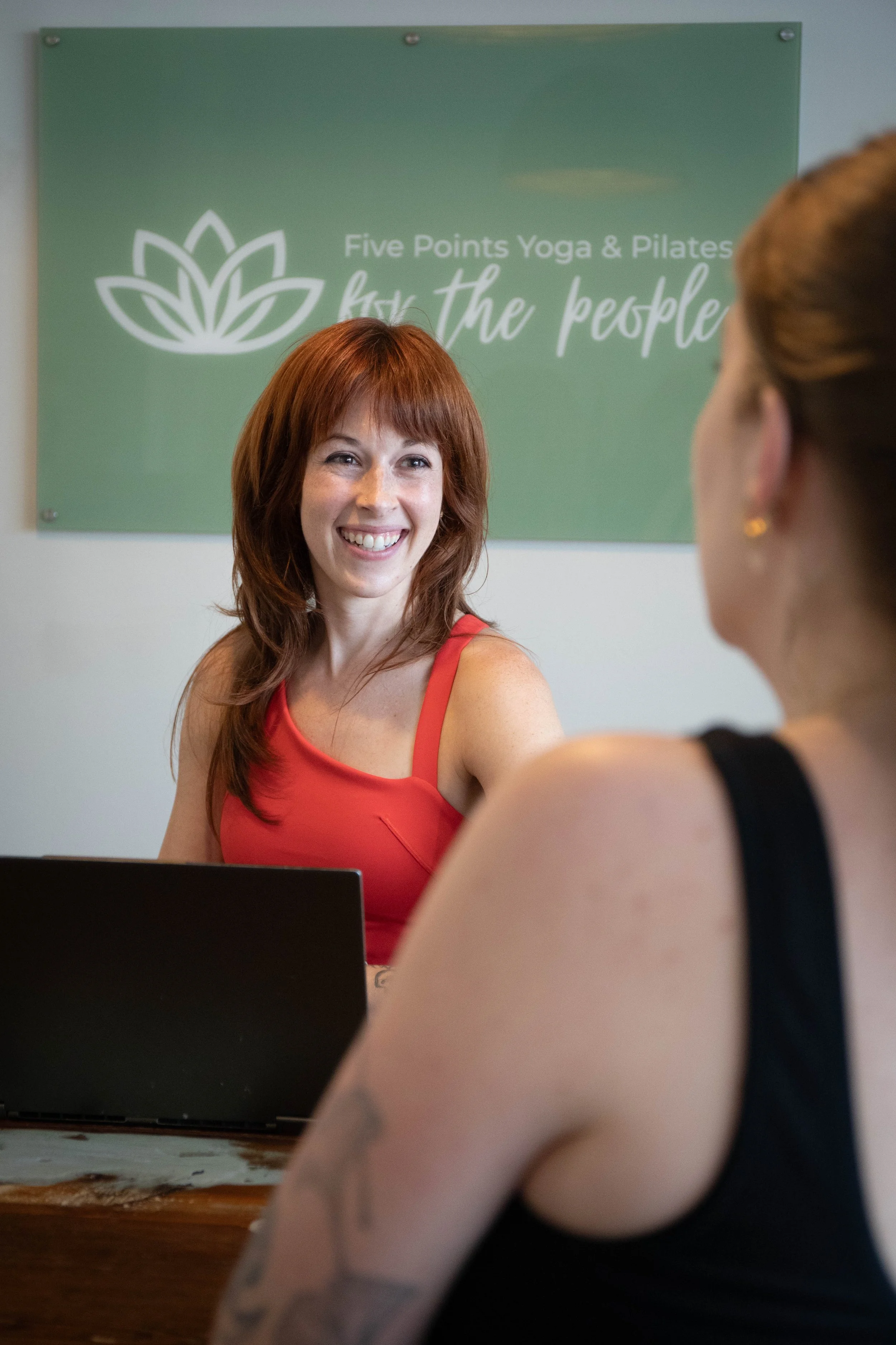 Pilates instructor smiling while talking to another instructor at the front desk