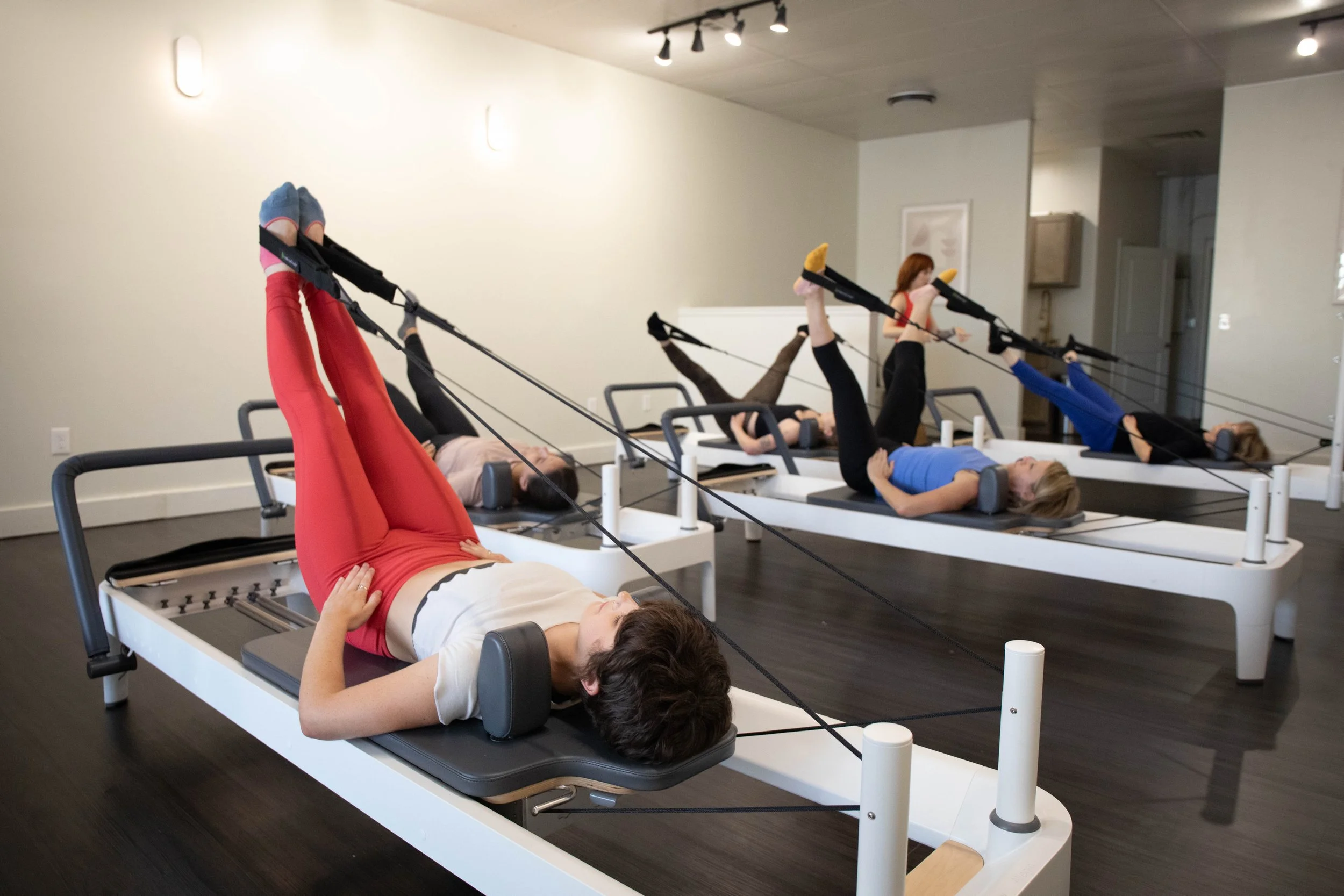 Students on four reformers, lying on their backs with feet in straps