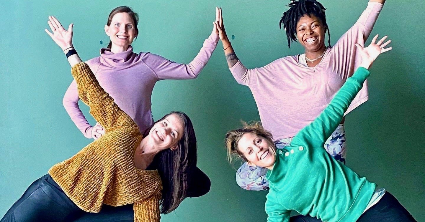 Four students standing with hands together to make the shape of a lotus, smiling