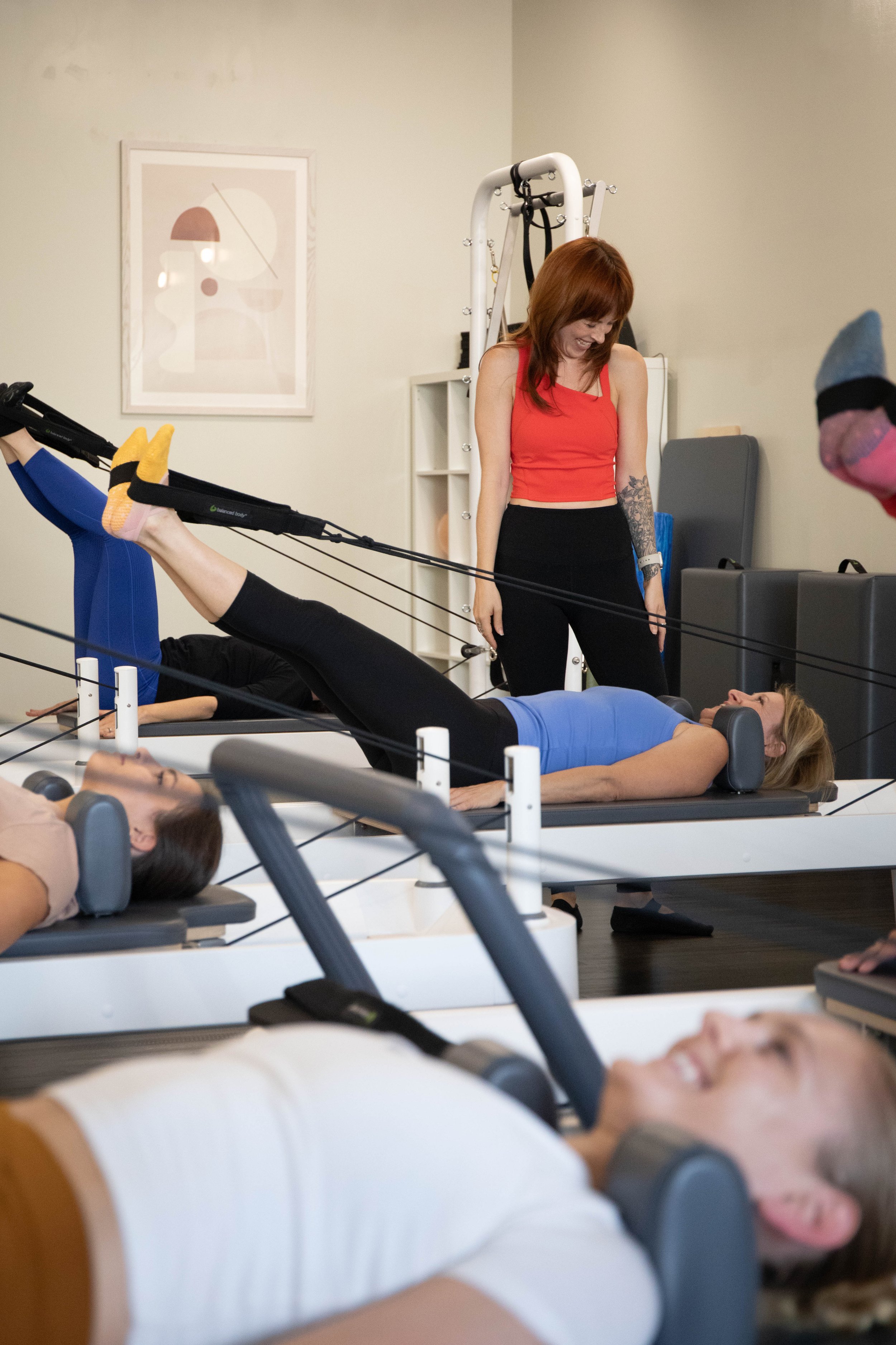 Pilates instrucotr smiles down at a student lying on their back on a reformer
