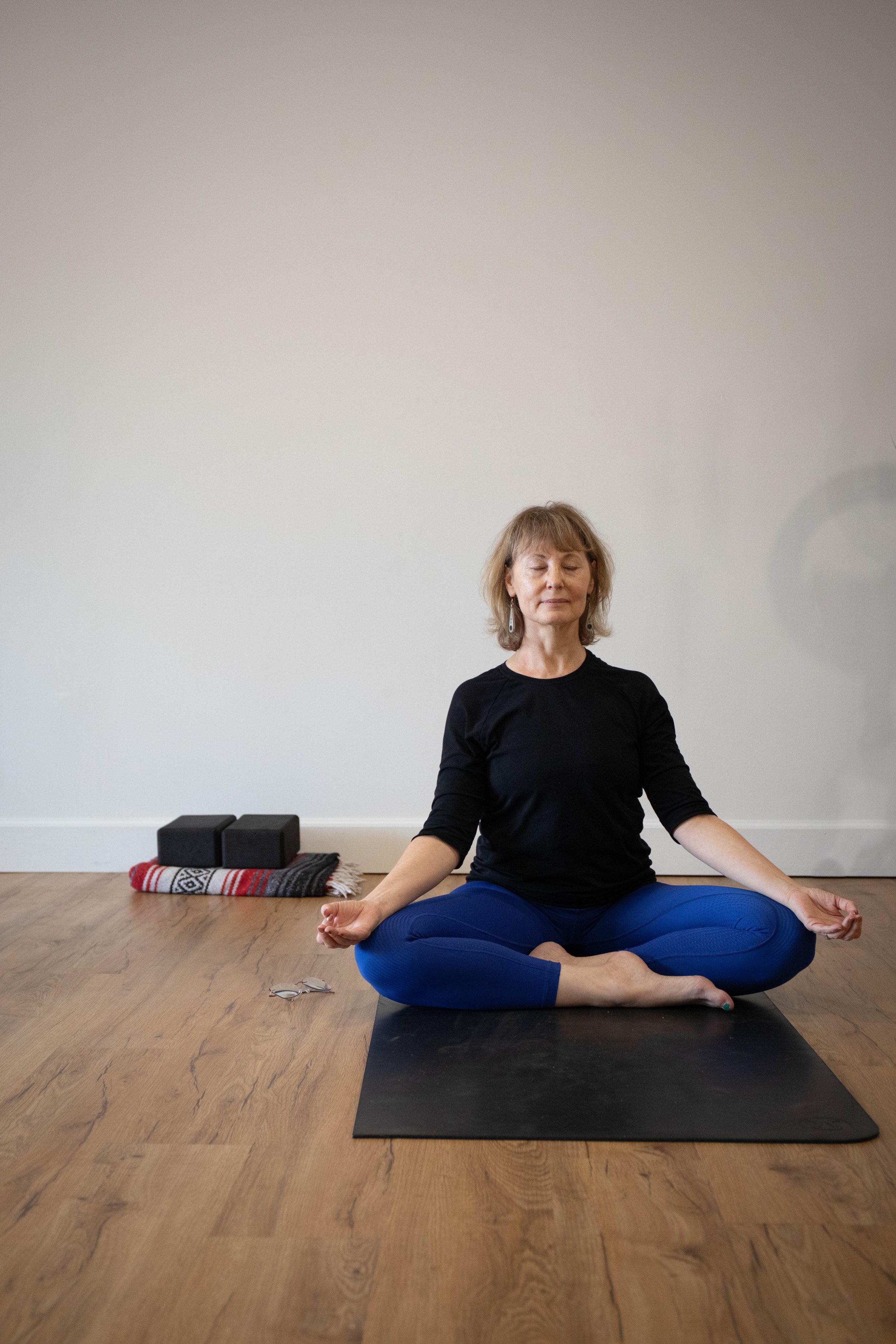 A woman sitting on a yoga mat in a meditative pose, with eyes closed