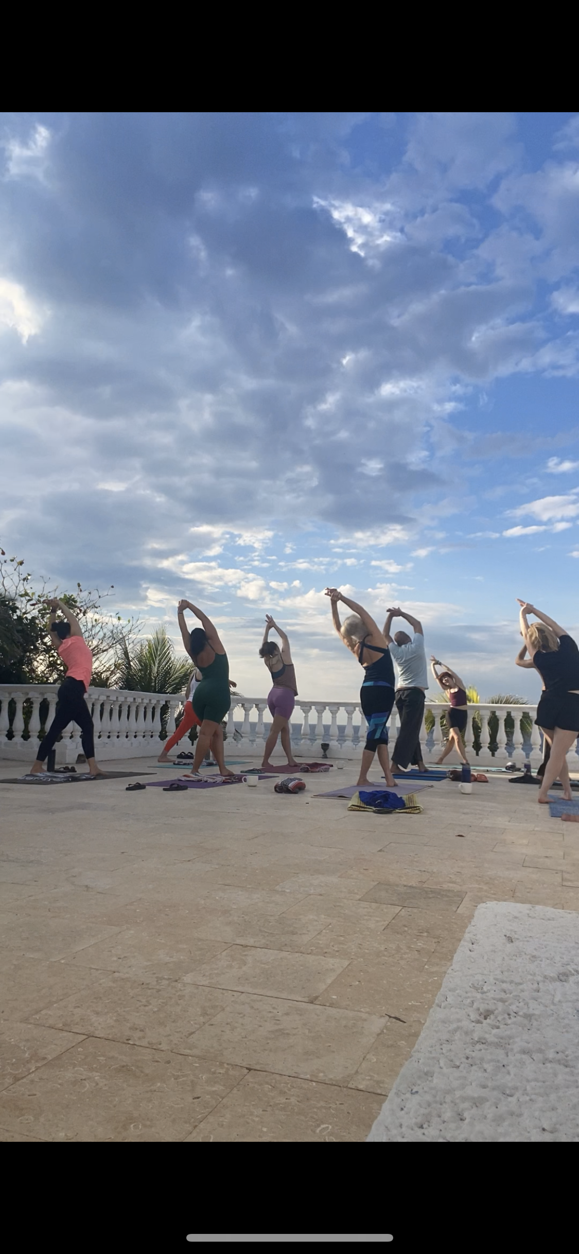 Retreat participants stretching arms overhead on a rooftop overlooking the ocean