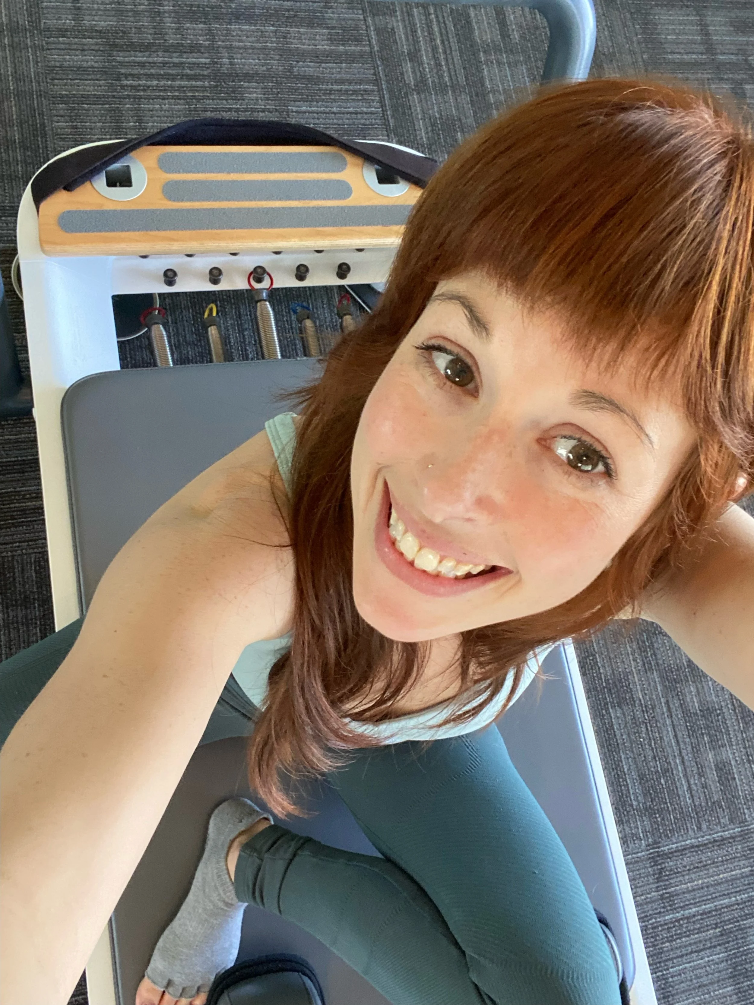 Pilates instructor takes a selfie from overhead while sitting on a reformer