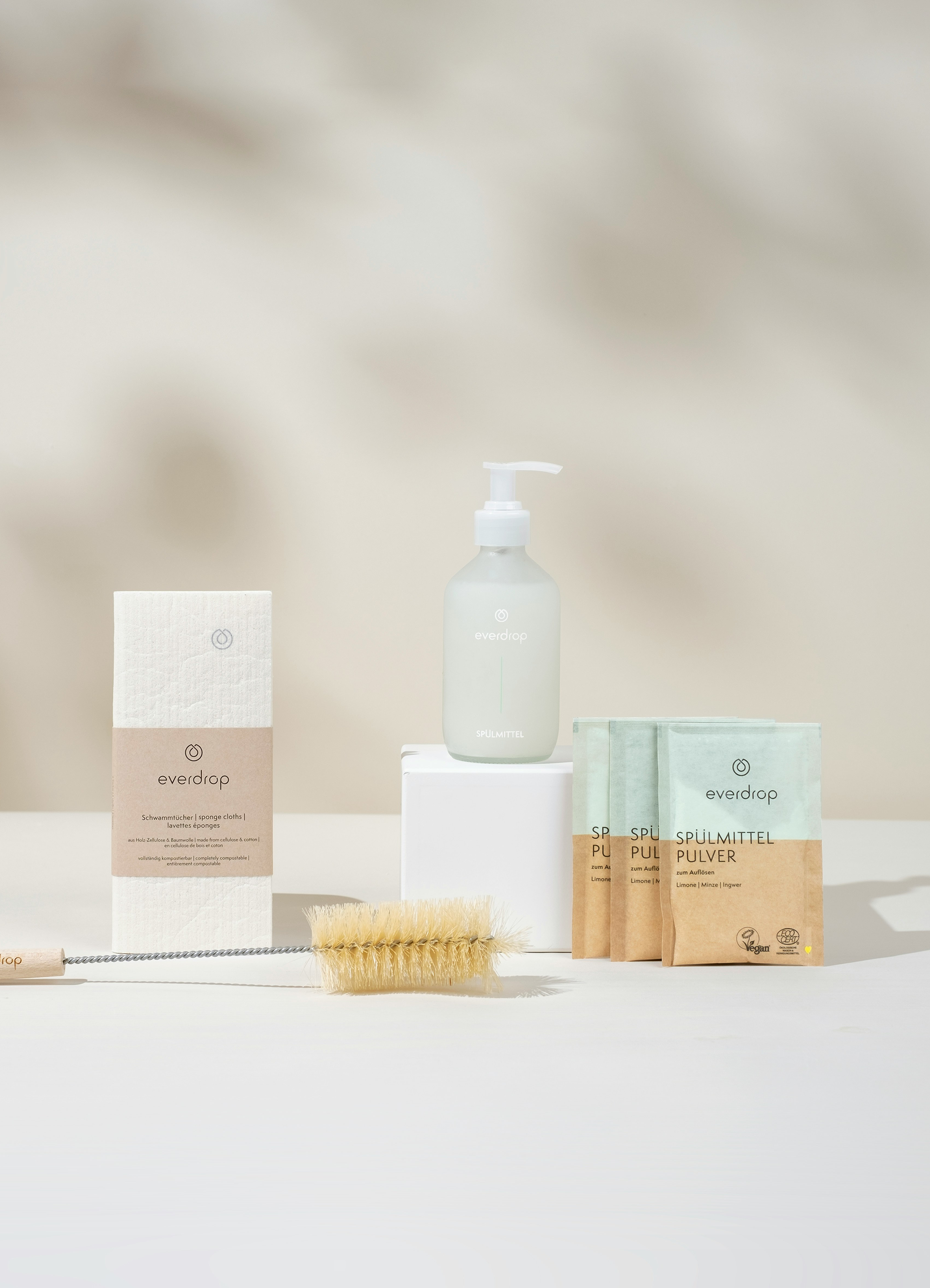 A collection of eco-friendly cleaning products including spare clothes, a spray bottle, and sachets of powder on a light background.