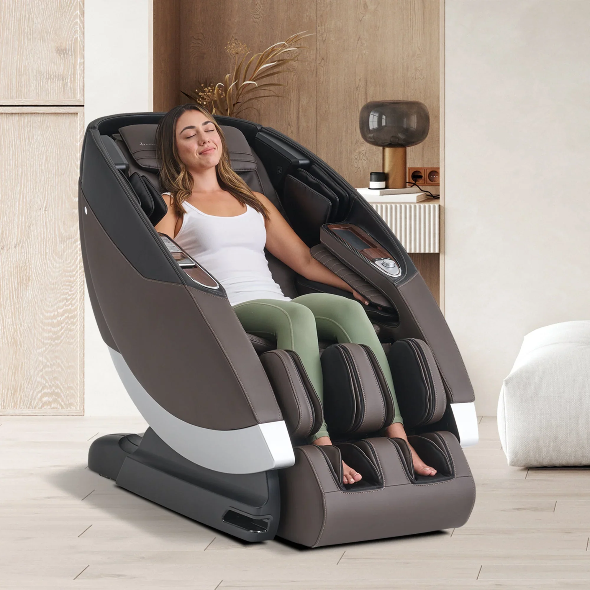 A woman relaxing in a modern massage chair with her eyes closed, located in a contemporary room with wooden wall panels and decorative items.