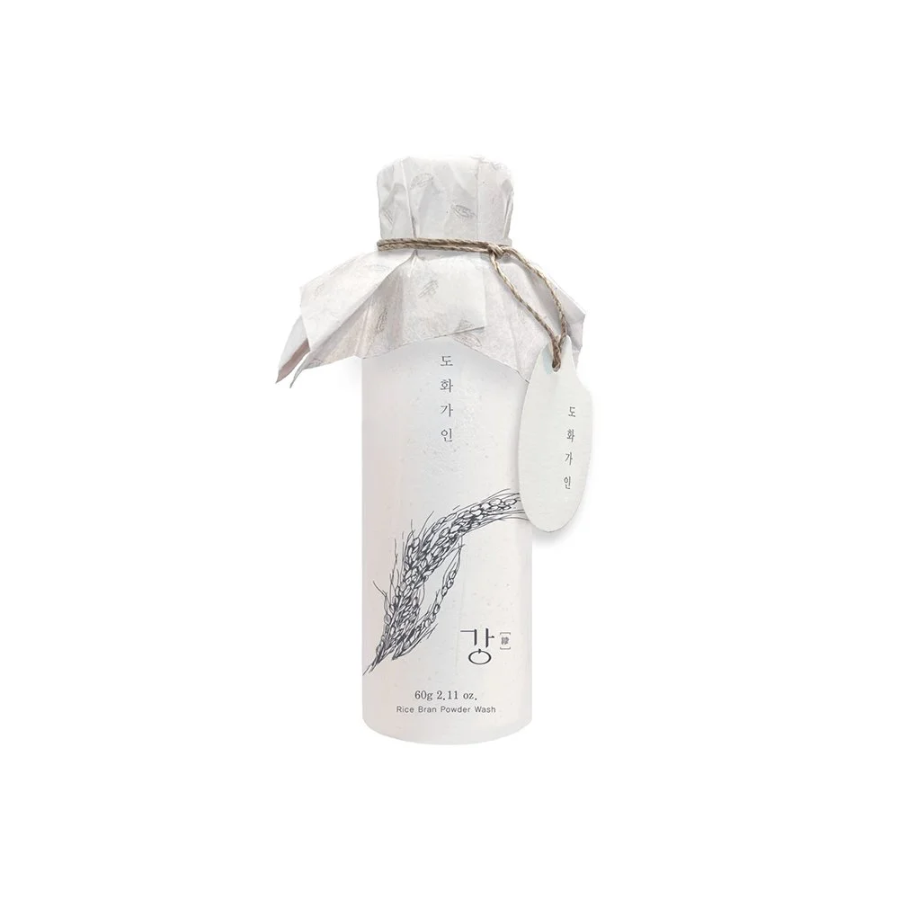 A white bottle labeled 'Rice Bran Powder Wash' with Korean writing, wrapped in paper with a string tie and a small tag attached.