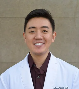 Portrait of Dr. Nelson Wong, DDS, smiling in a white dental coat in front of a neutral background.