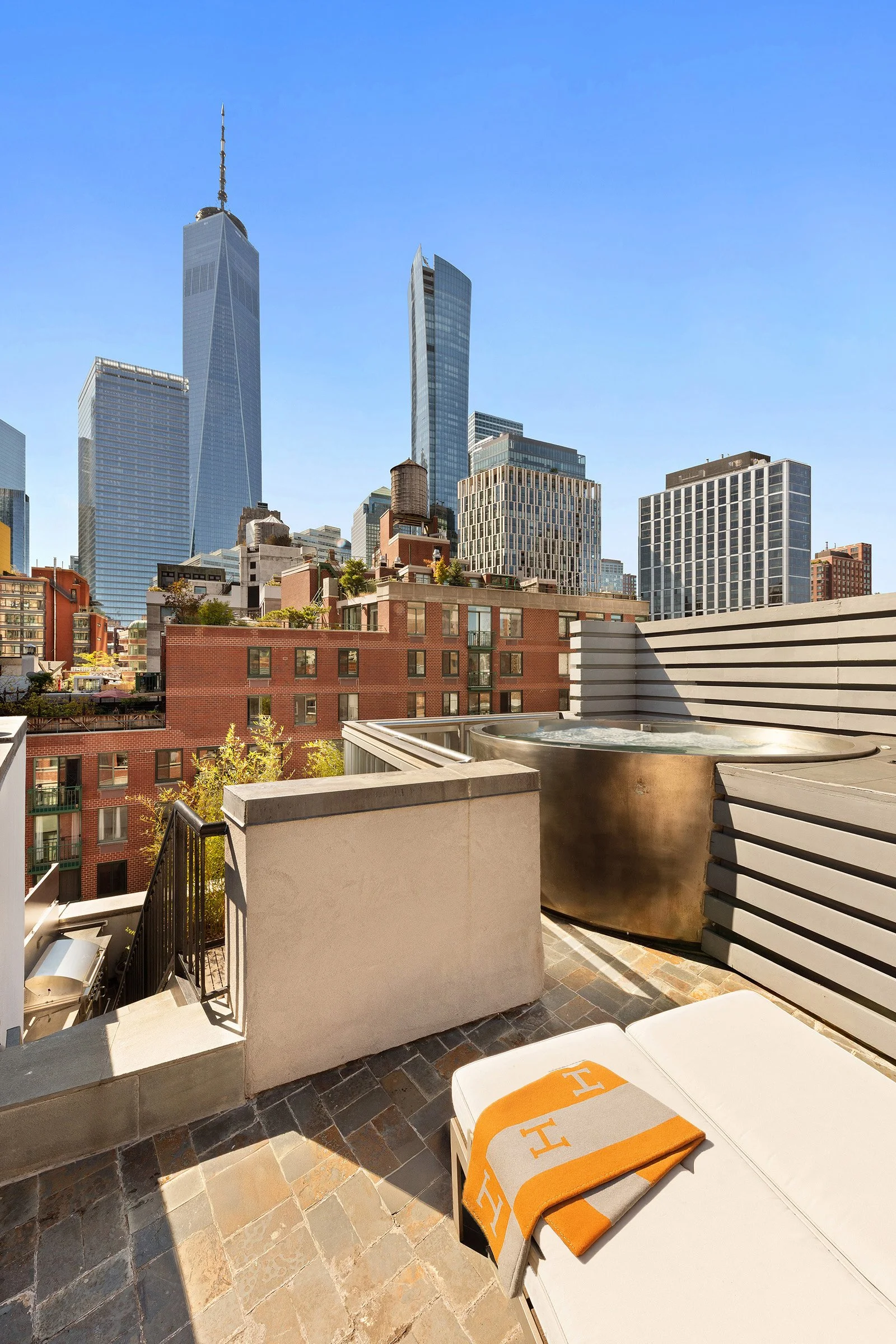 City skyline view from a rooftop balcony with tall skyscrapers and a lounge chair draped with Hermès towels at 152 Reade Street in Tribeca.