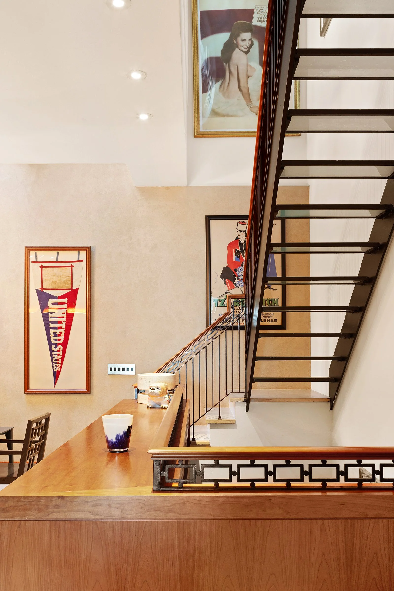 Interior of a building with framed art posters on the walls, a staircase leading to the upper floor, and a wooden counter with decorative items at 152 Reade Street in Tribeca.