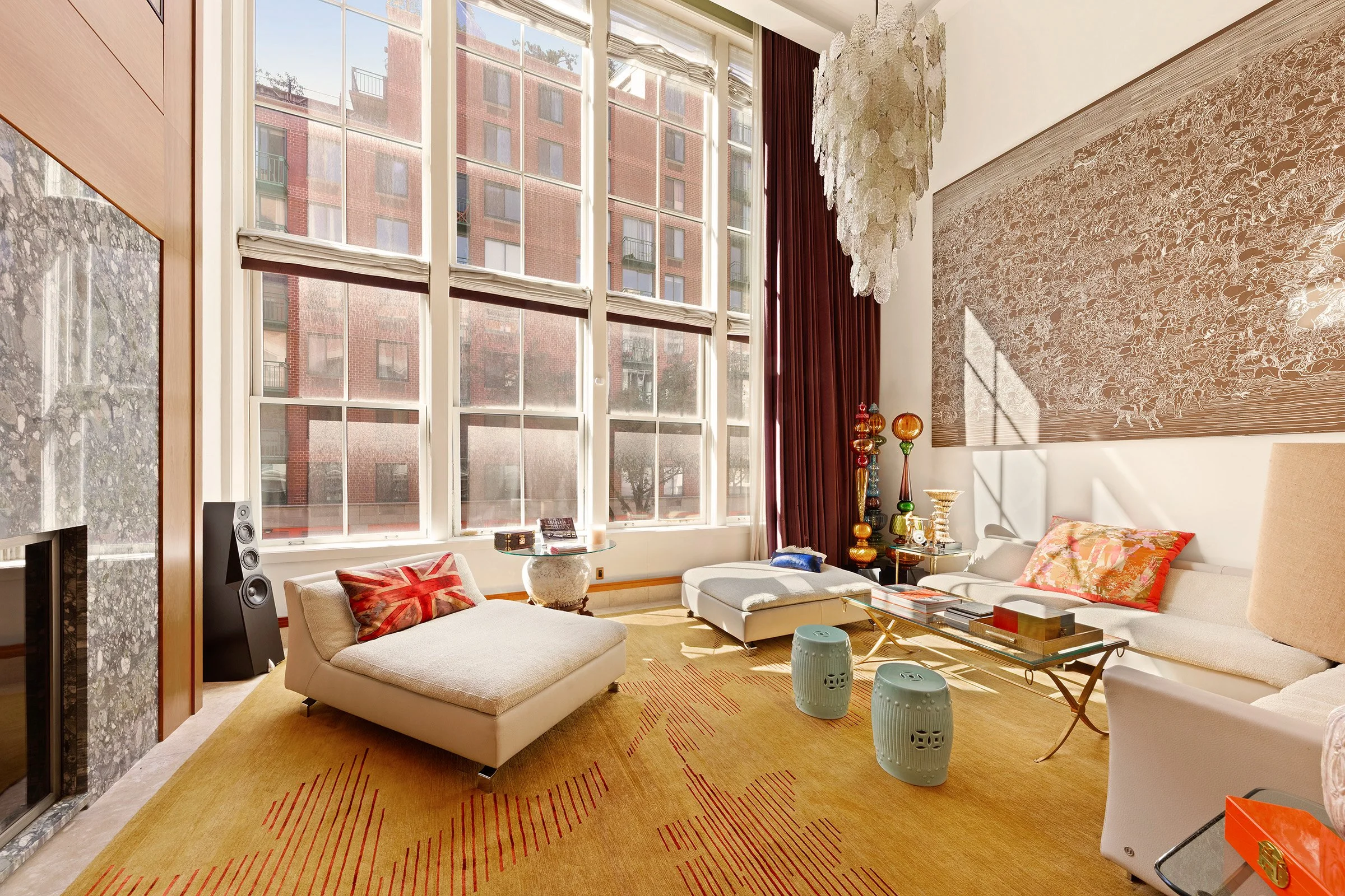 A modern living room with large windows, beige sofas, a glass coffee table, colorful decorative pillows, and textured artwork on the wall, filled with natural sunlight at 152 Reade Street in Tribeca.