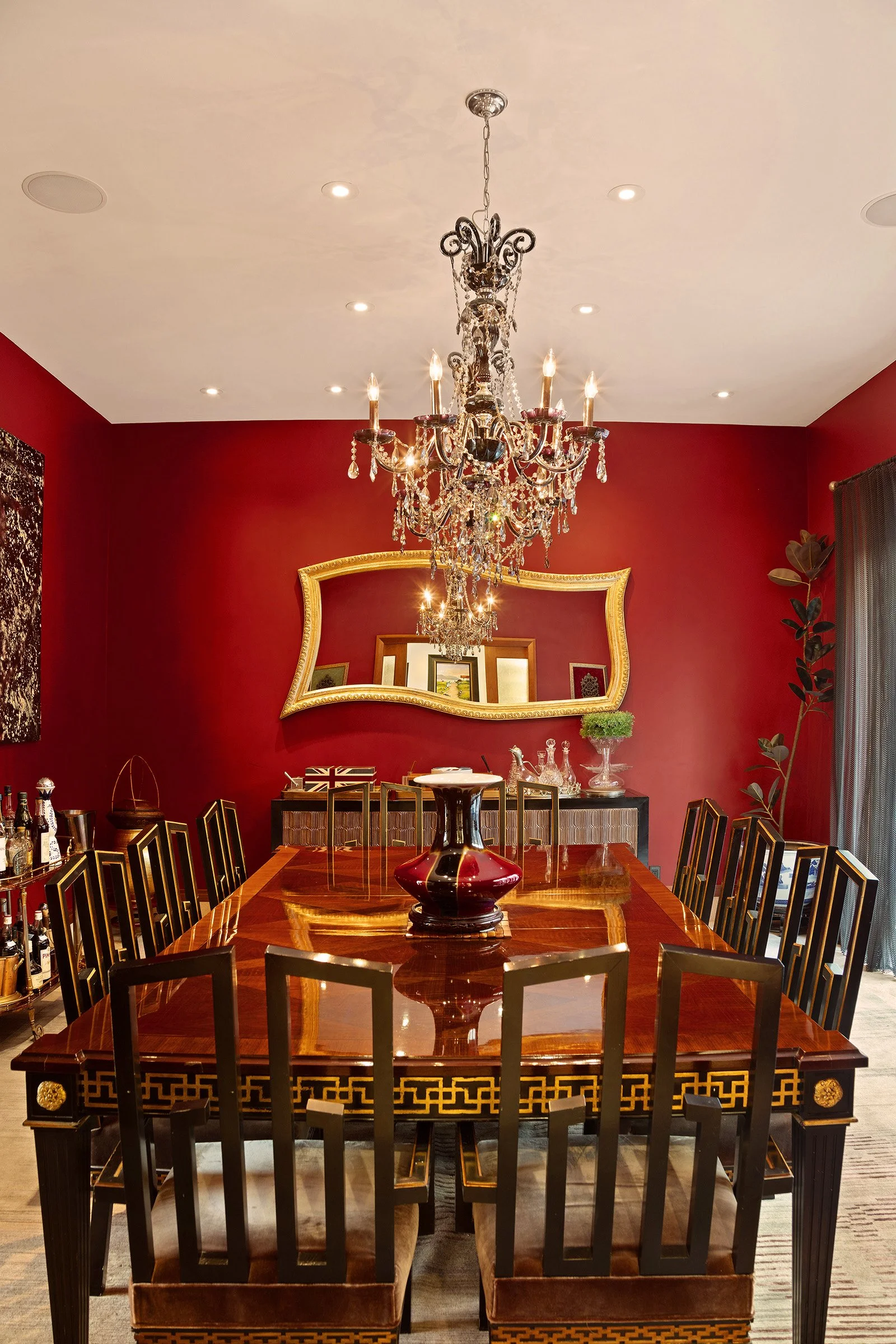 A luxurious dining room with red walls, a large wooden table, a crystal chandelier, a large mirror, and decorative accents at 152 Reade Street in Tribeca.