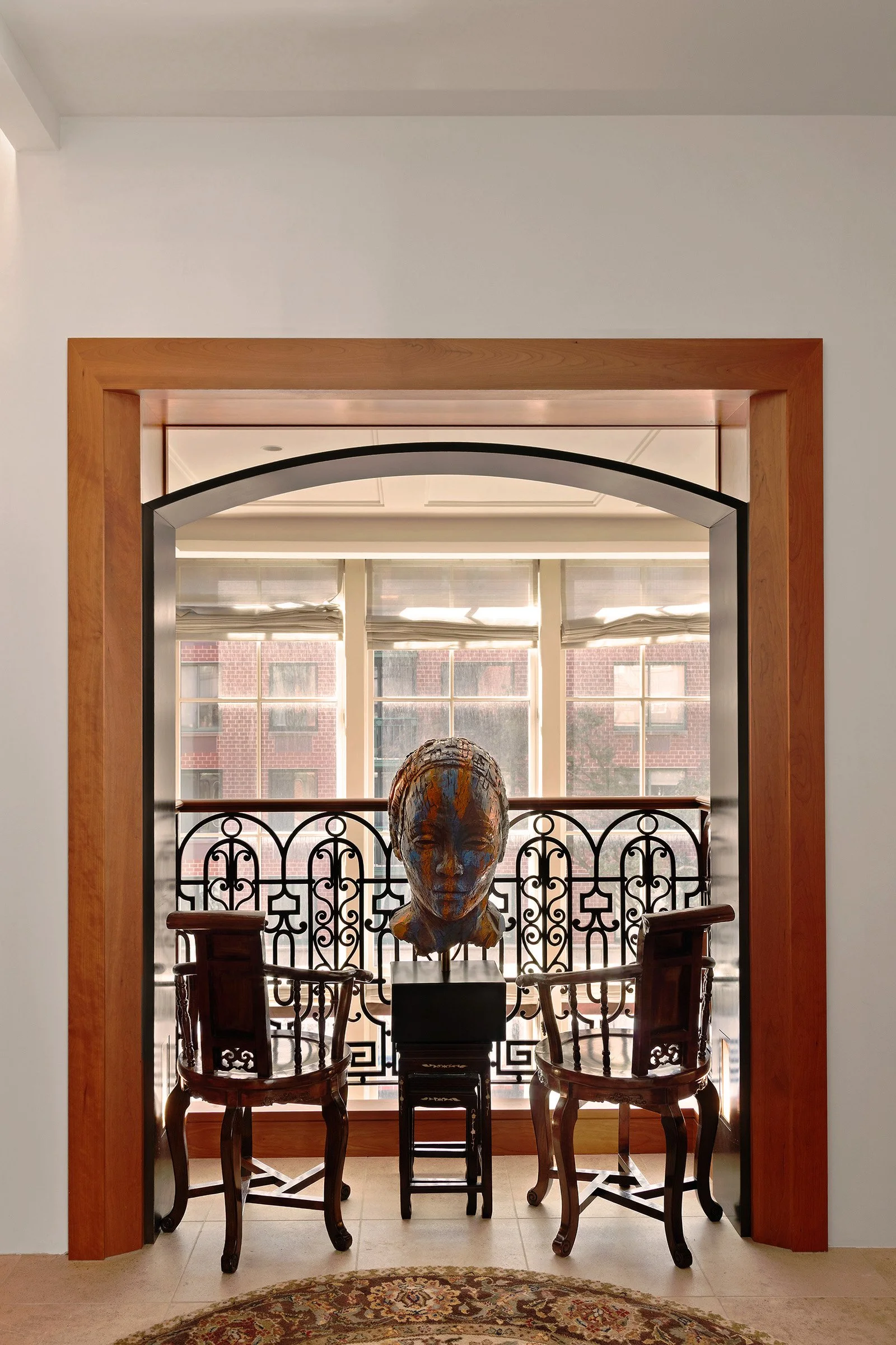 Interior view of a room with a decorative archway, two wooden chairs, a sculpture of a human head, and a patterned rug at 152 Reade Street in Tribeca.